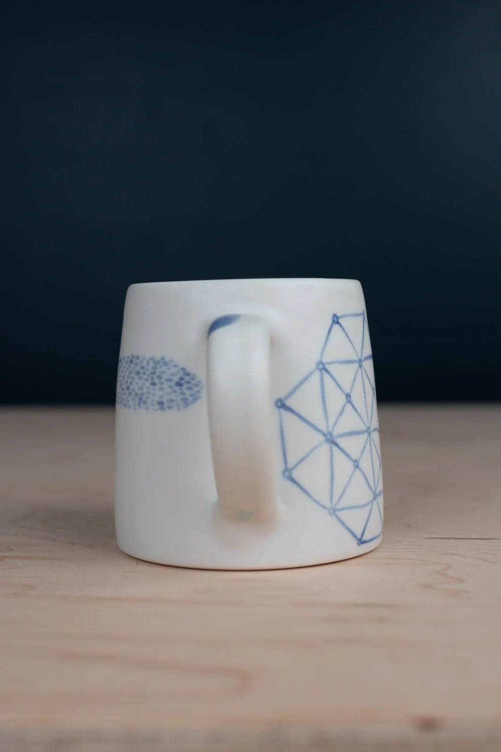 Hand-thrown porcelain mug with blue illustrations painted on the surface.