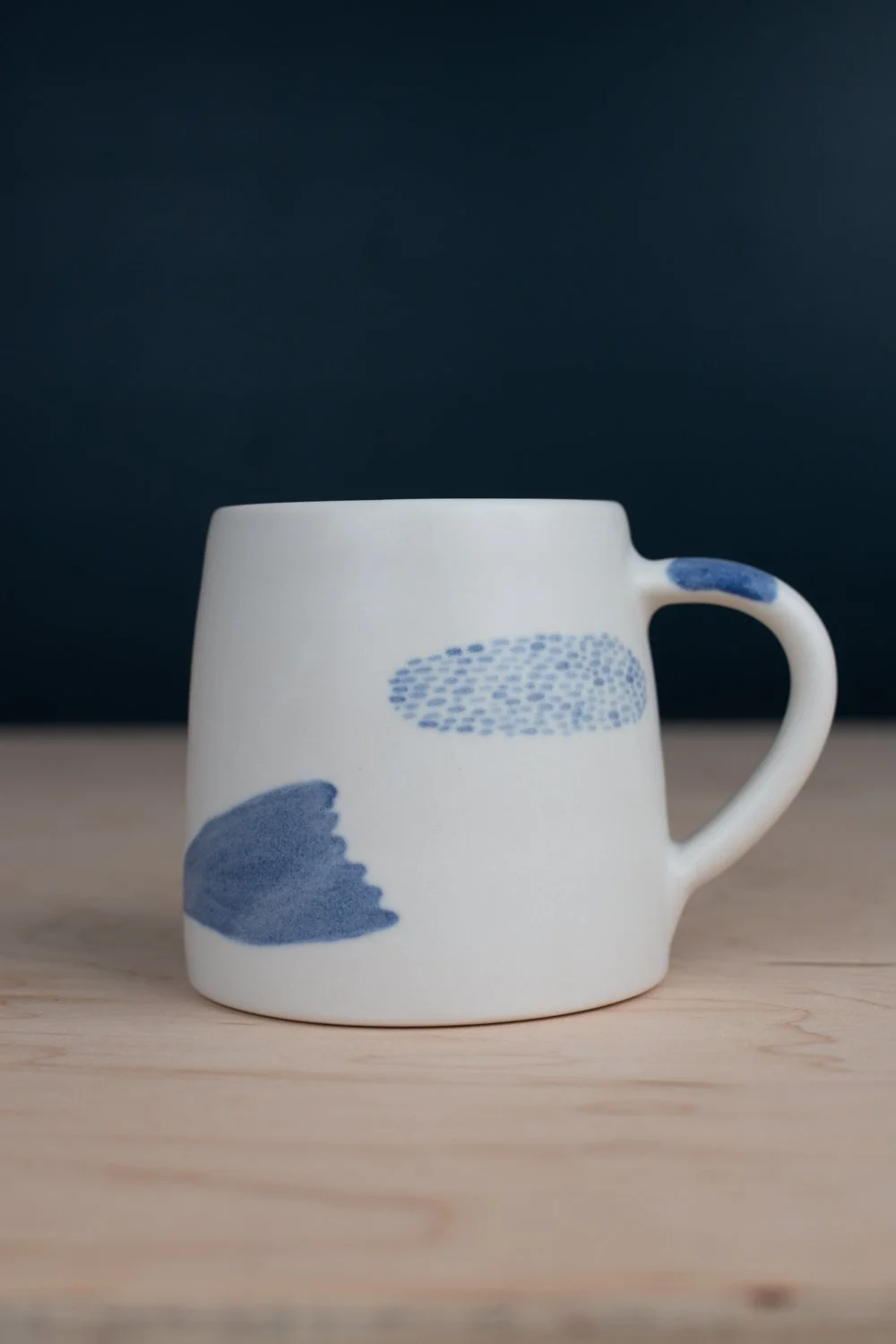 Hand-thrown porcelain mug with blue illustrations painted on the surface.