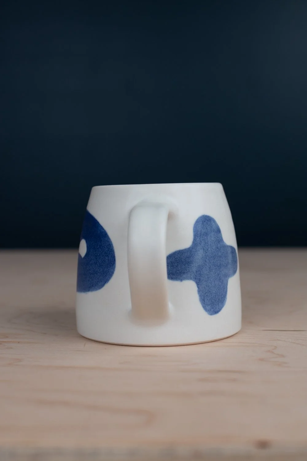 Hand-thrown porcelain mug with blue illustrations painted on the surface.