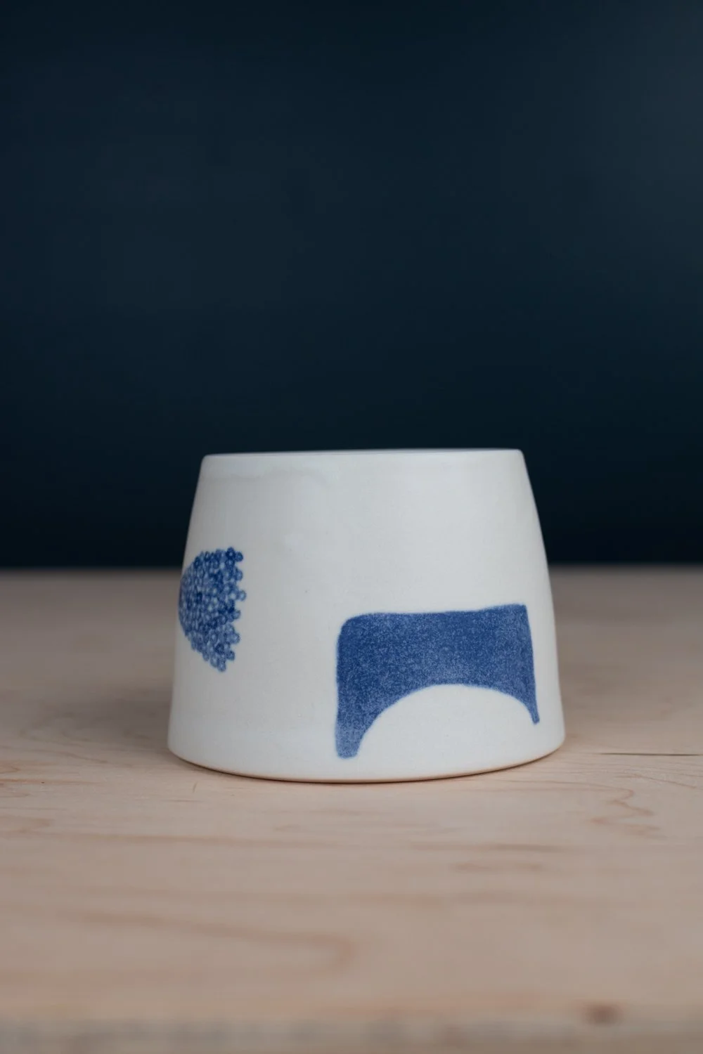 Hand-thrown porcelain mug with blue illustrations painted on the surface.