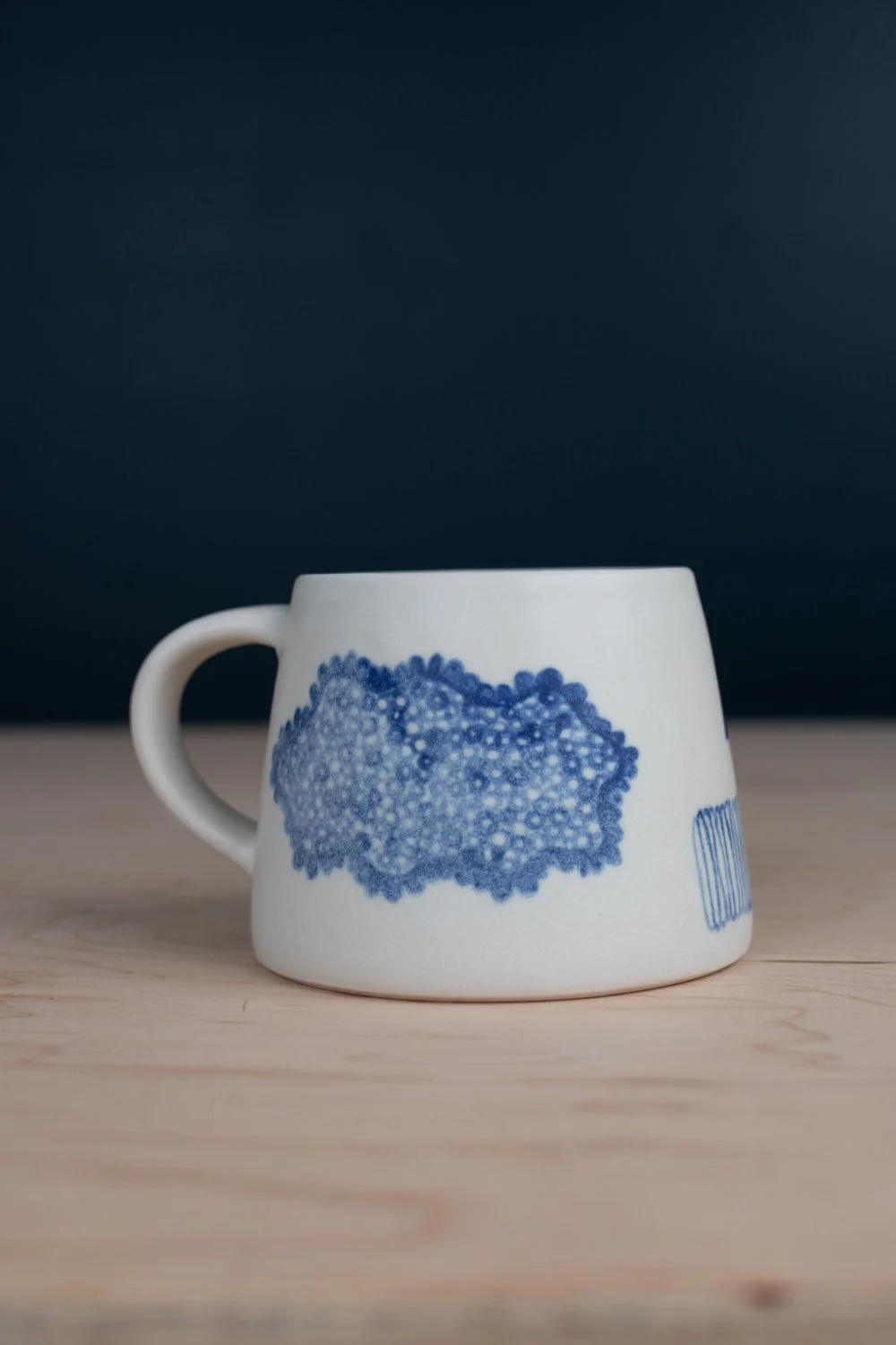 Hand-thrown porcelain mug with blue illustrations painted on the surface.