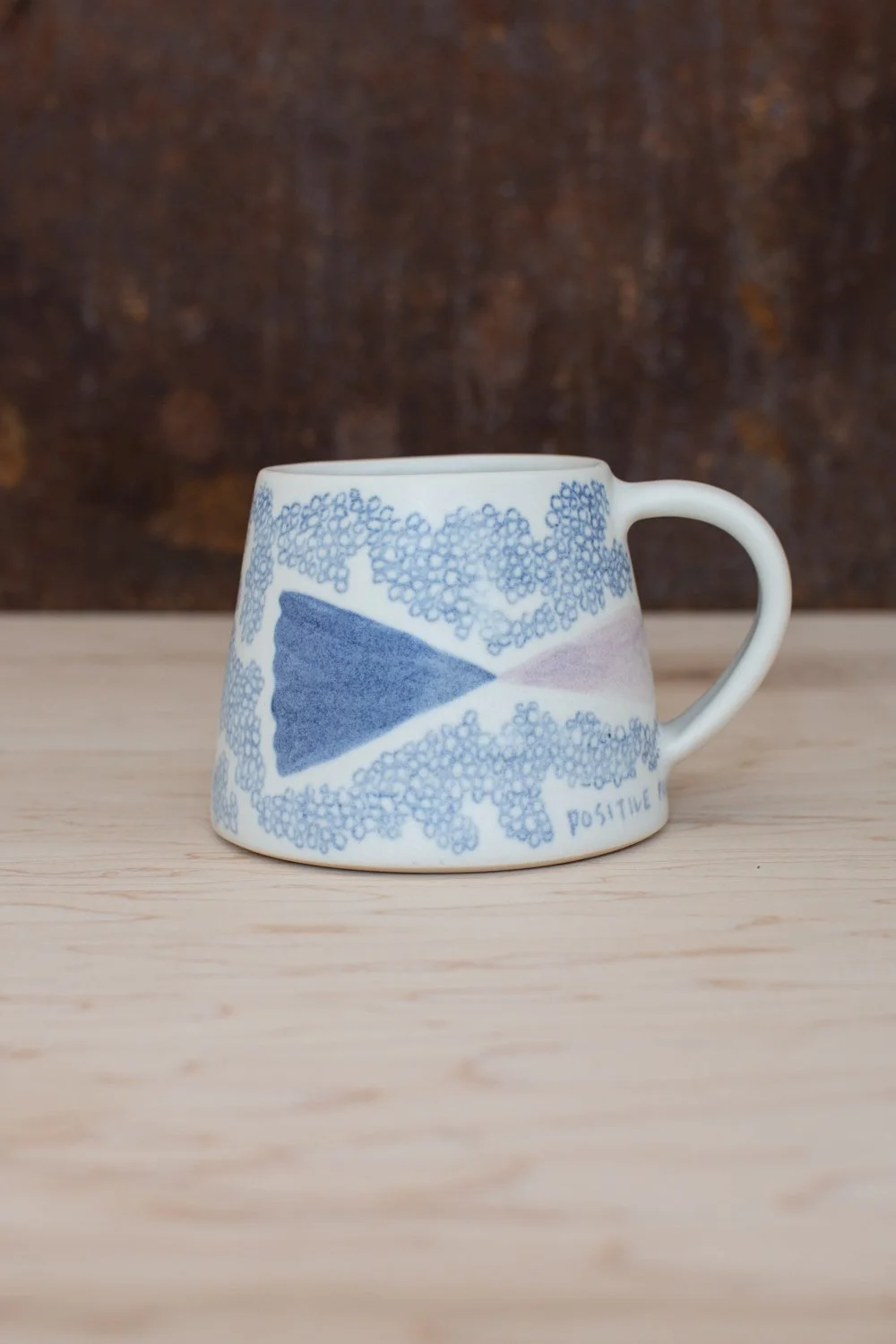 Hand-thrown porcelain mug with blue illustrations painted on the surface.