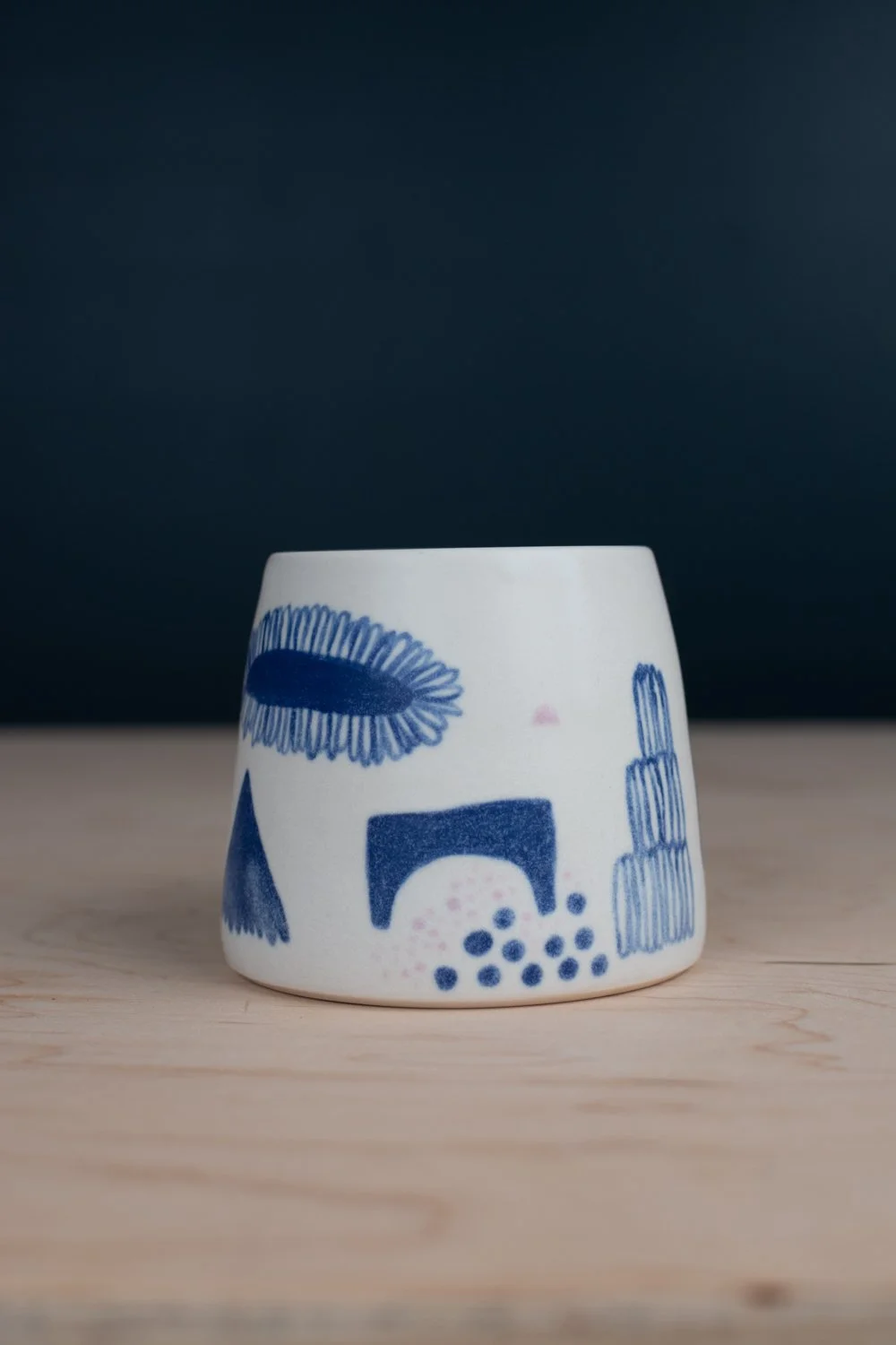 Hand-thrown porcelain mug with blue illustrations painted on the surface.
