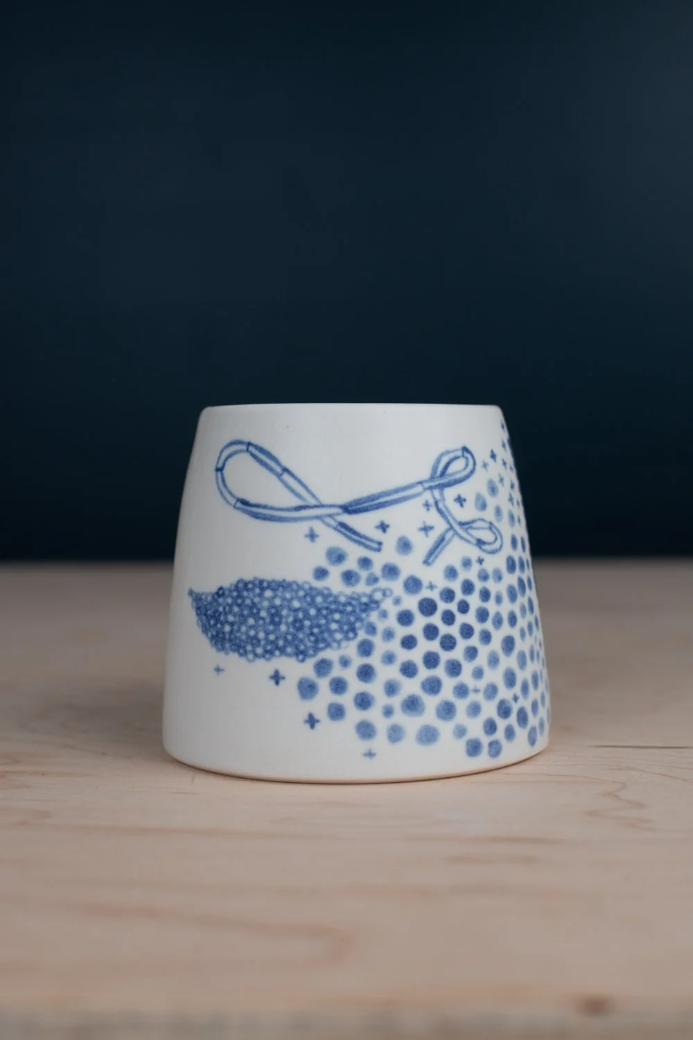 Hand-thrown porcelain mug with blue illustrations painted on the surface.