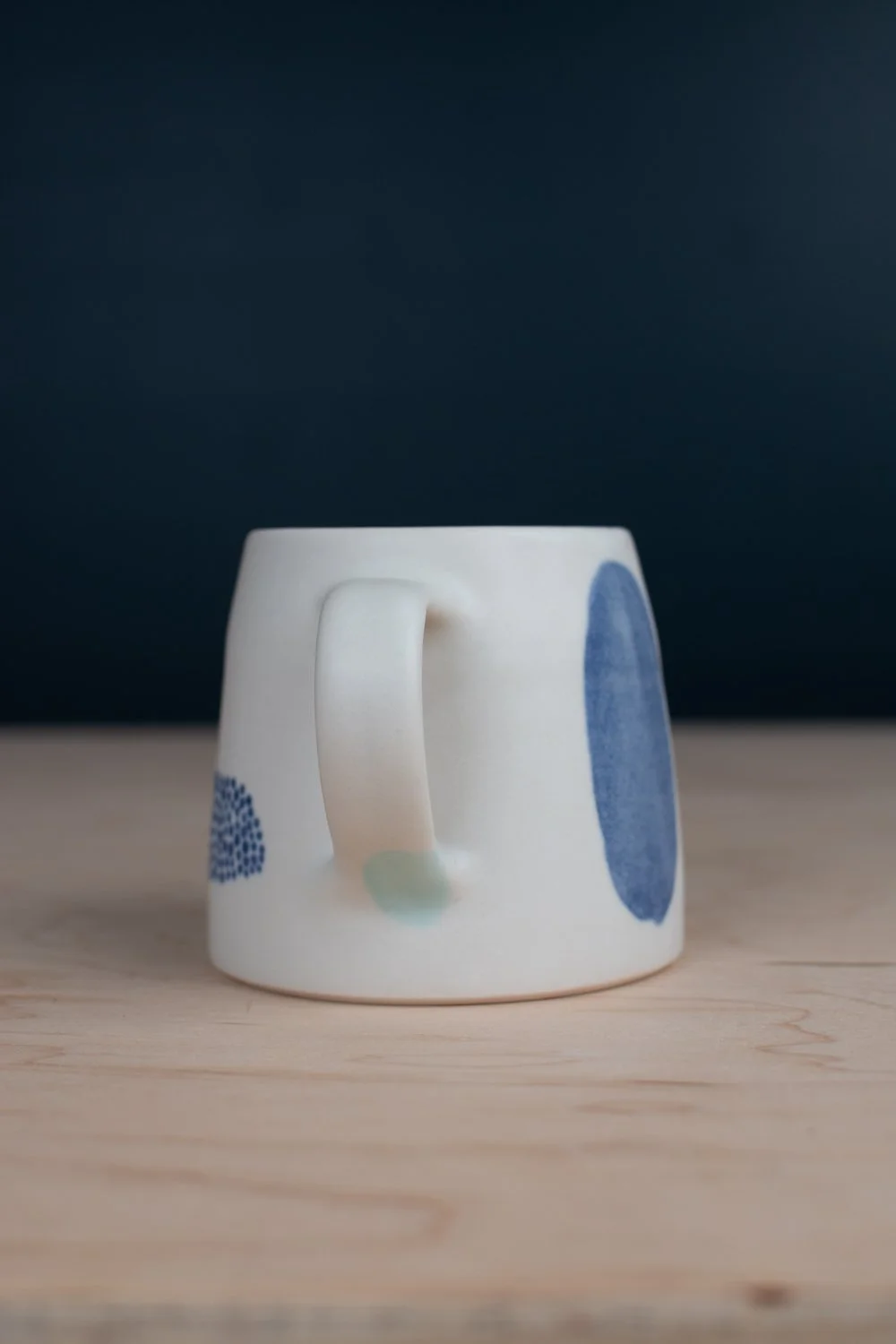 Hand-thrown porcelain mug with blue illustrations painted on the surface.
