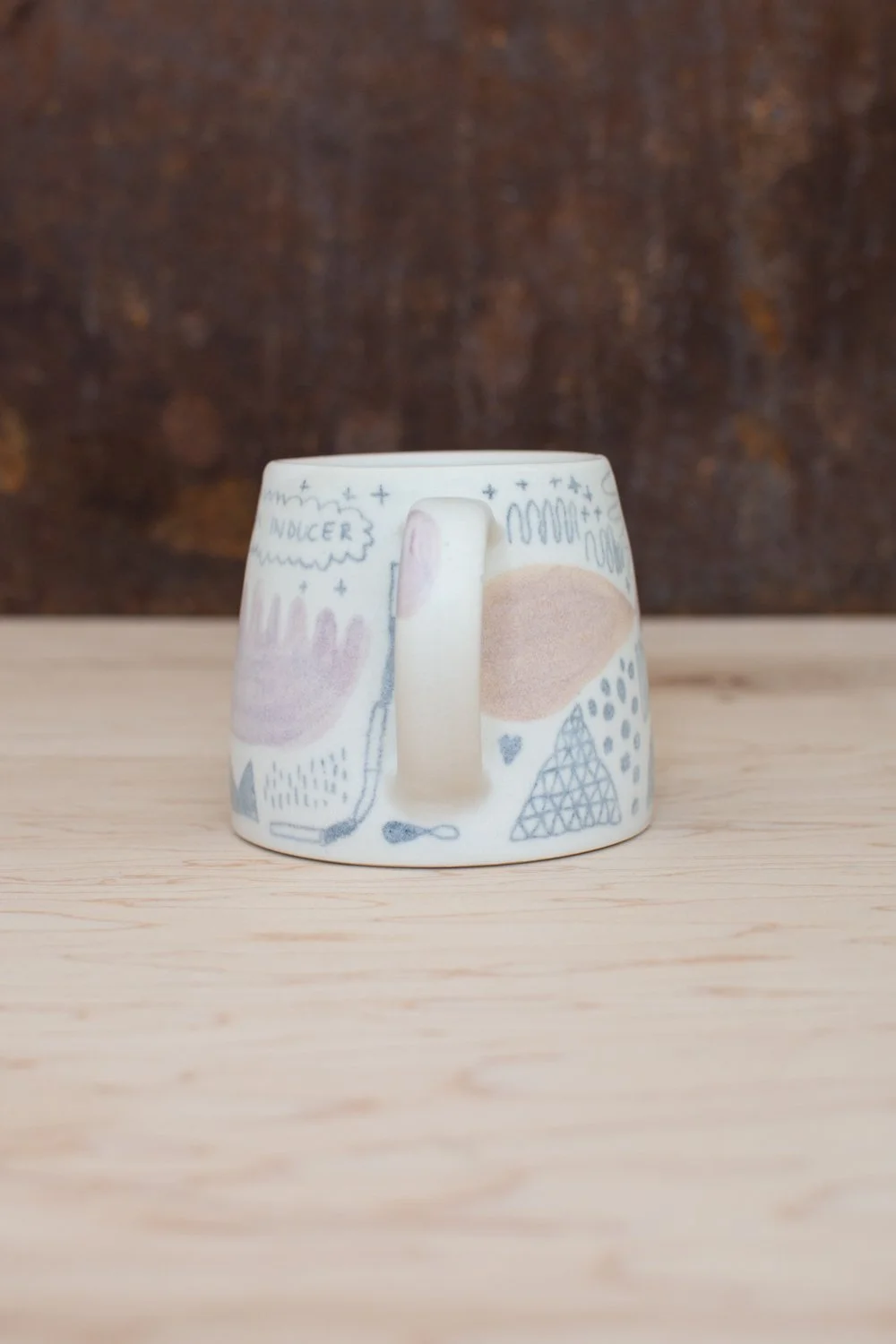Hand-thrown porcelain mug with pink and ochre illustrations.