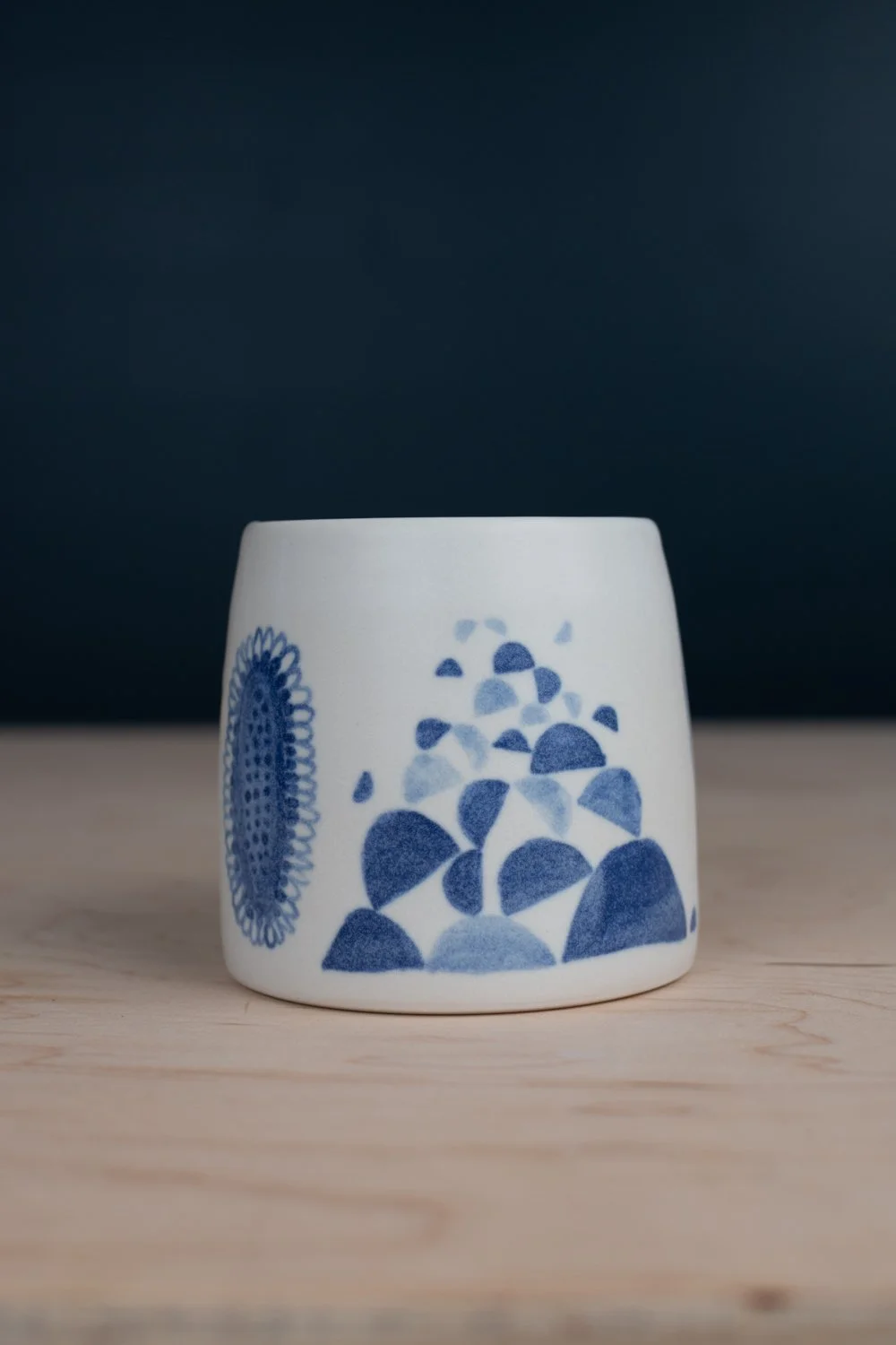 Hand-thrown porcelain mug with blue illustrations painted on the surface.