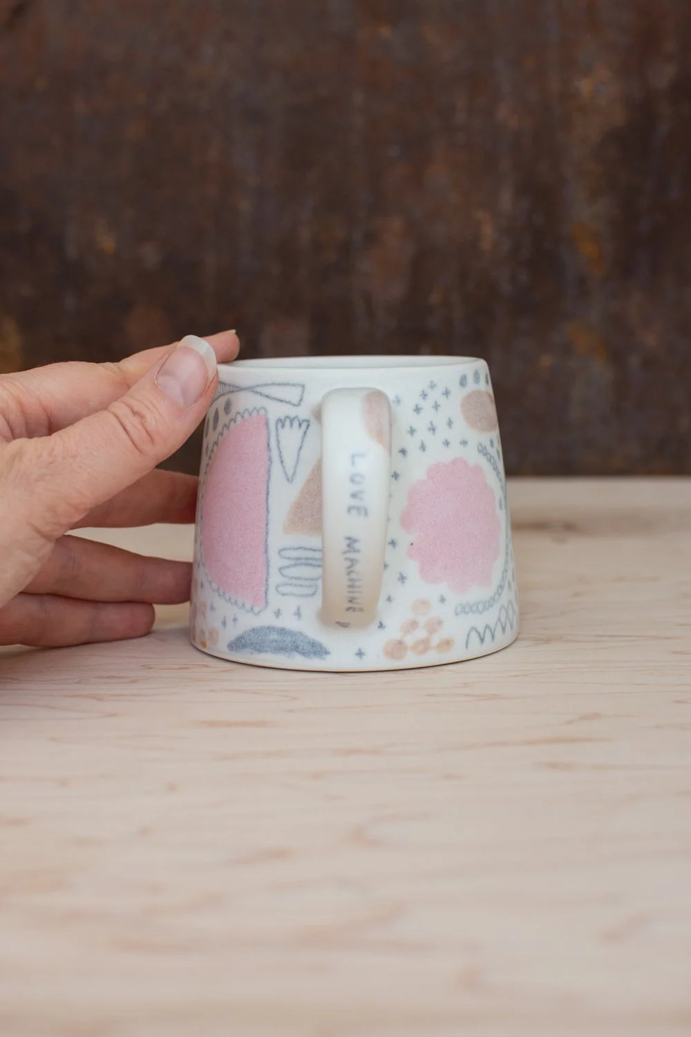 Hand-thrown porcelain mug with pink and ochre illustrations painted on the surface.