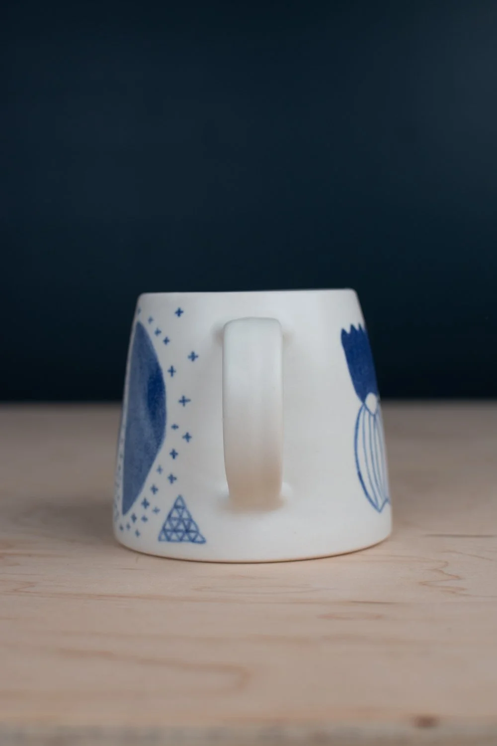 Hand-thrown porcelain mug with blue illustrations painted on the surface.