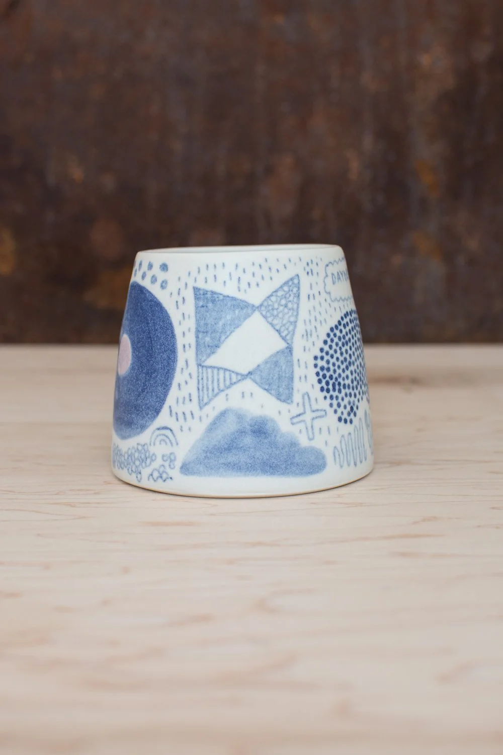 Hand-thrown porcelain mug with blue and purple illustrations painted on the surface.