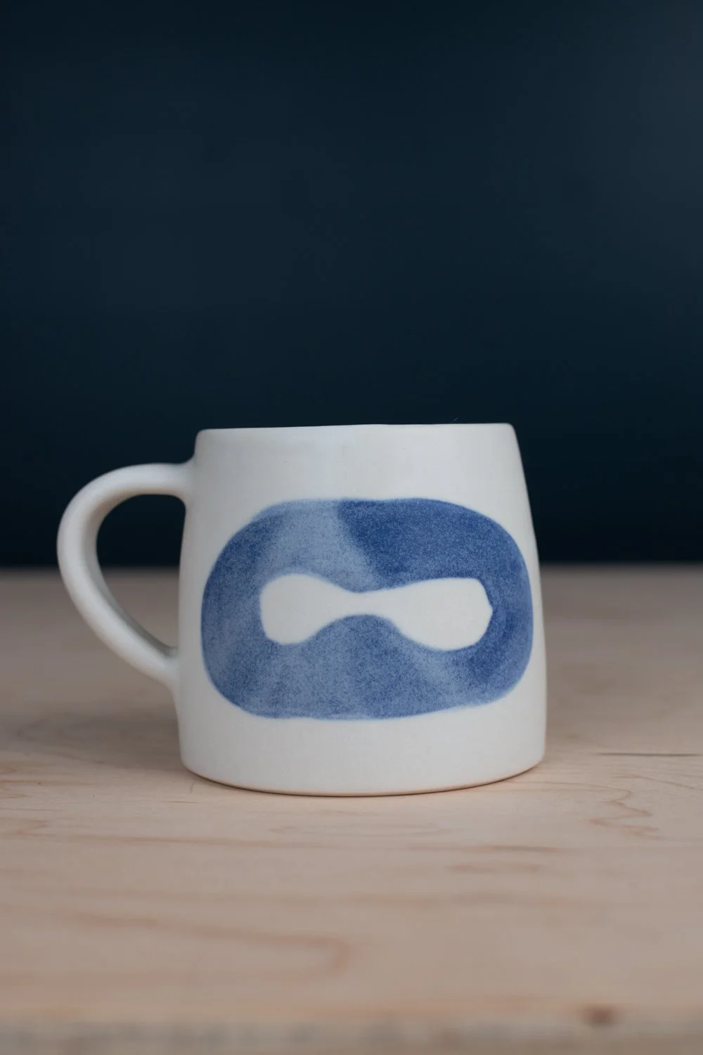 Hand-thrown porcelain mug with blue illustrations painted on the surface.