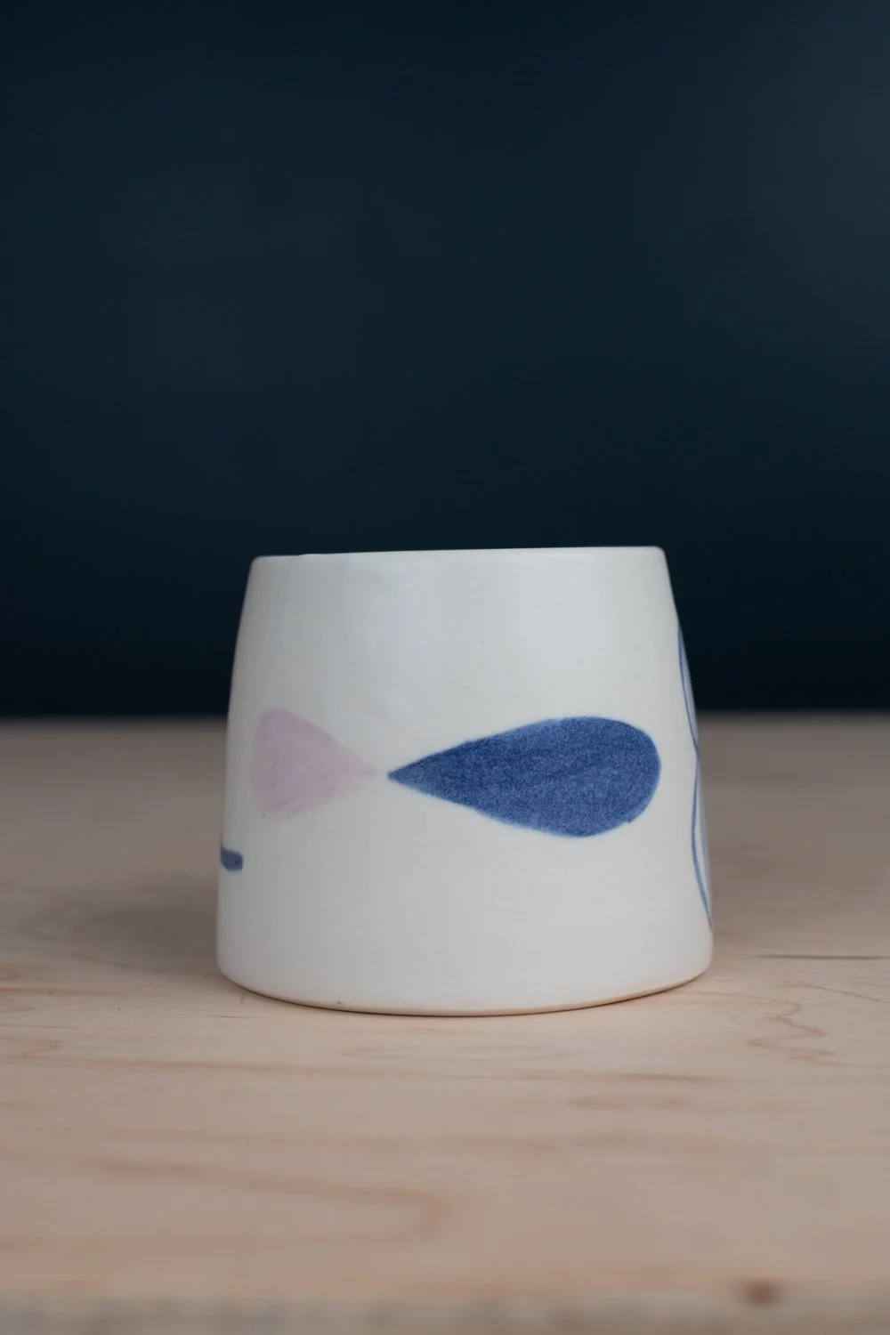 Hand-thrown porcelain mug with blue illustrations painted on the surface.