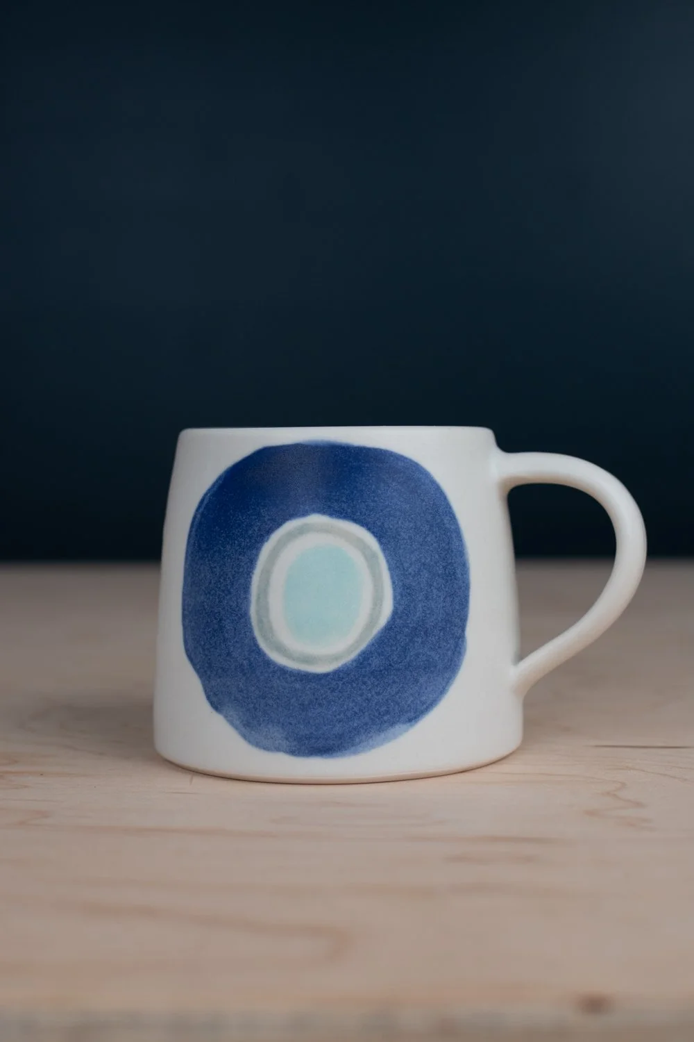 Hand-thrown porcelain mug with blue illustrations painted on the surface.