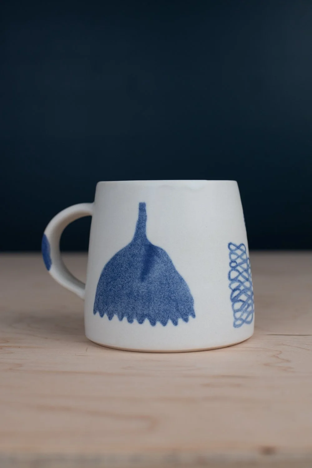 Hand-thrown porcelain mug with blue illustrations painted on the surface.