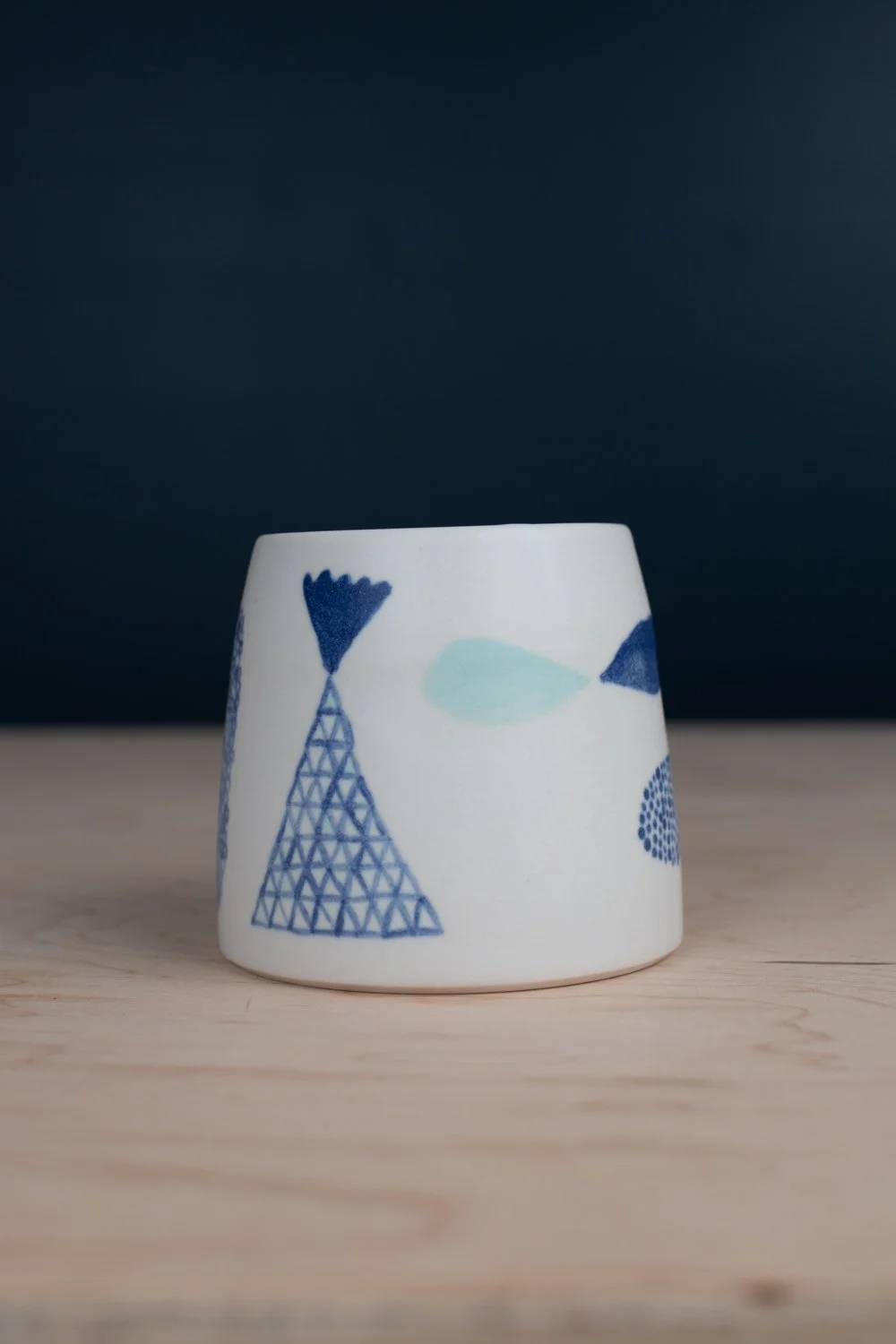 Hand-thrown porcelain mug with blue illustrations painted on the surface.