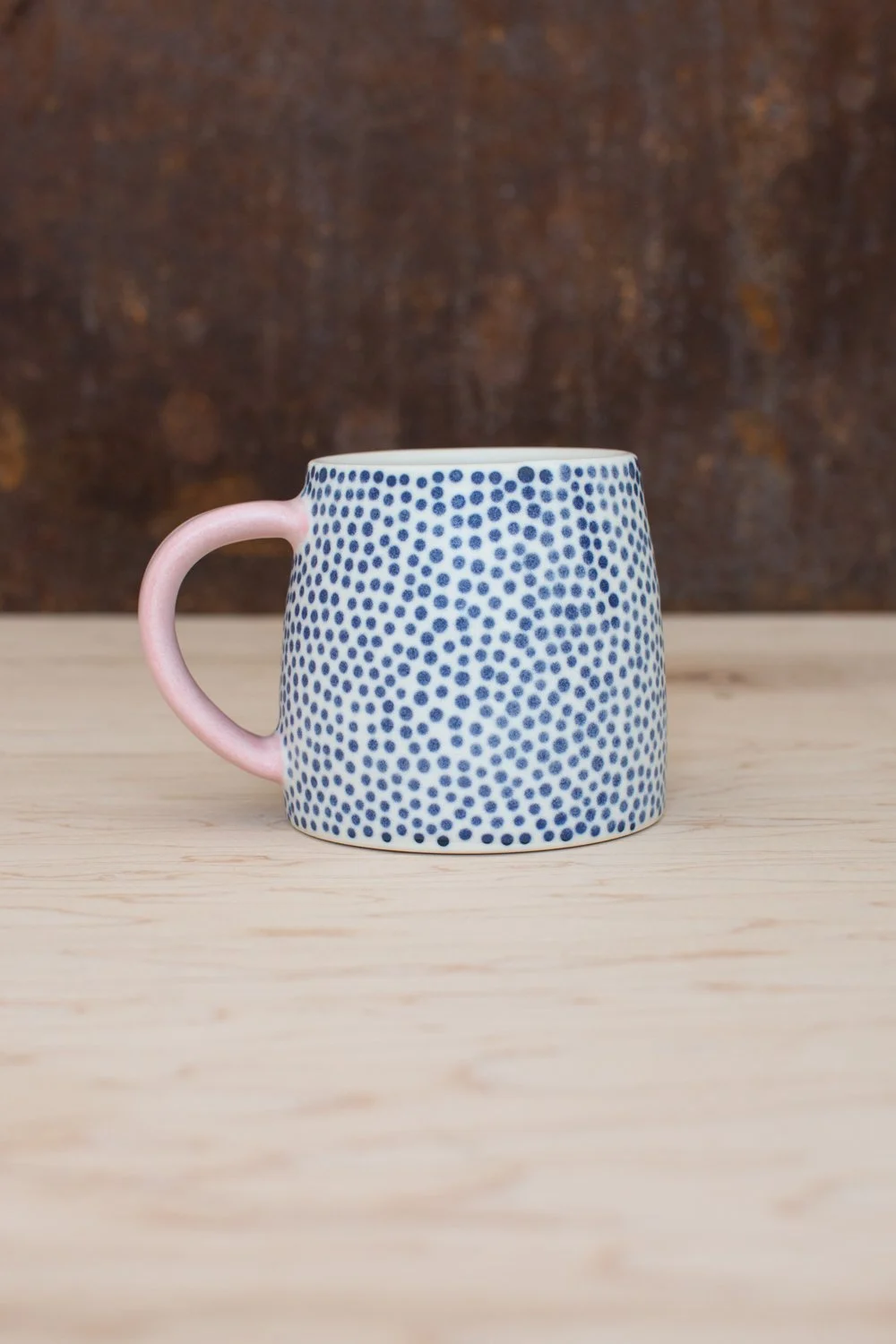 Hand-thrown porcelain mug with blue dots and a pink handle.