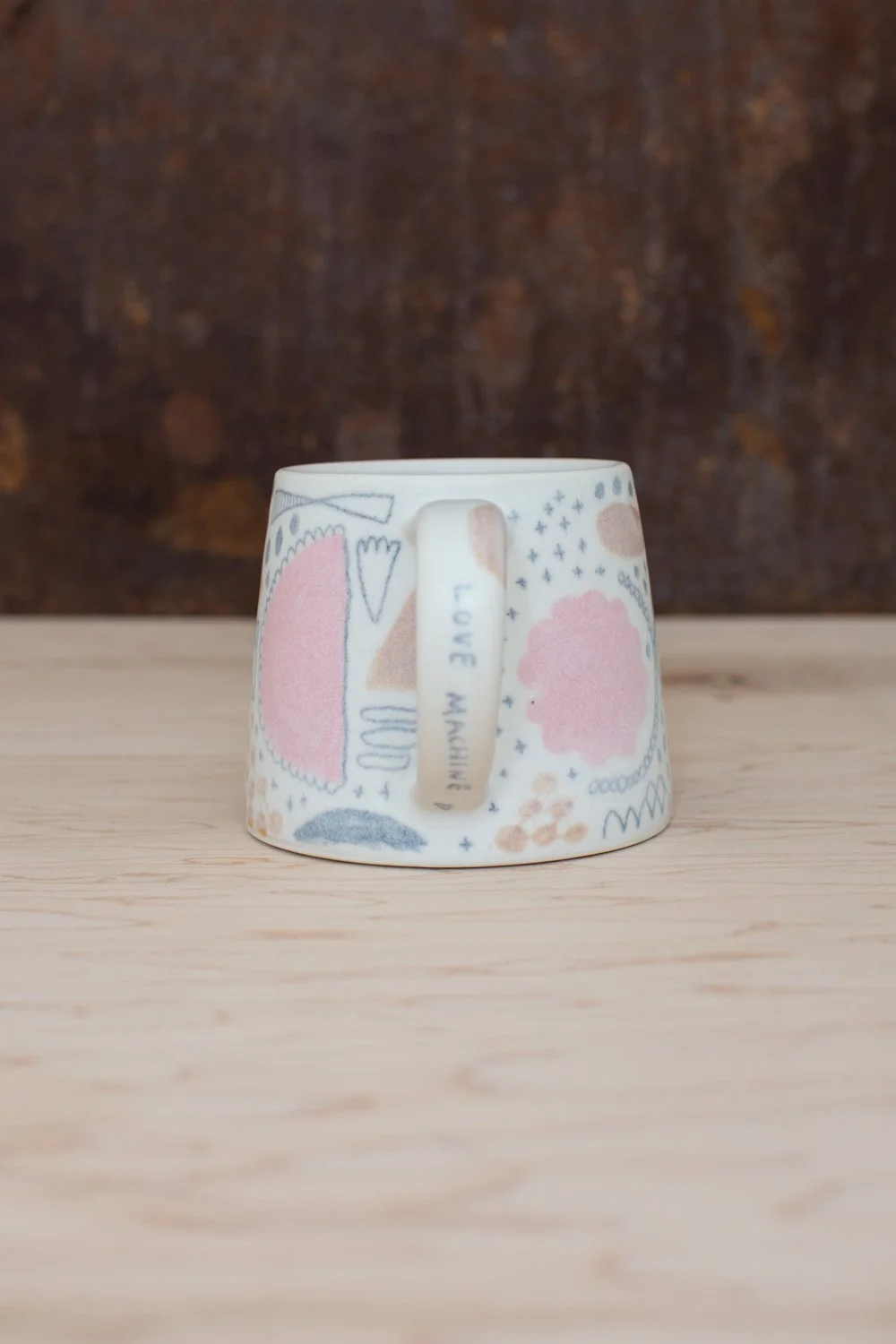 Hand-thrown porcelain mug with pink and ochre illustrations painted on the surface.