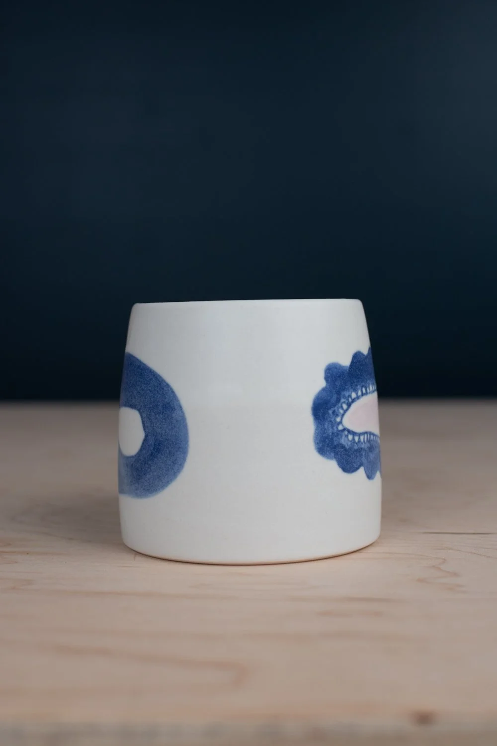 Hand-thrown porcelain mug with blue illustrations painted on the surface.