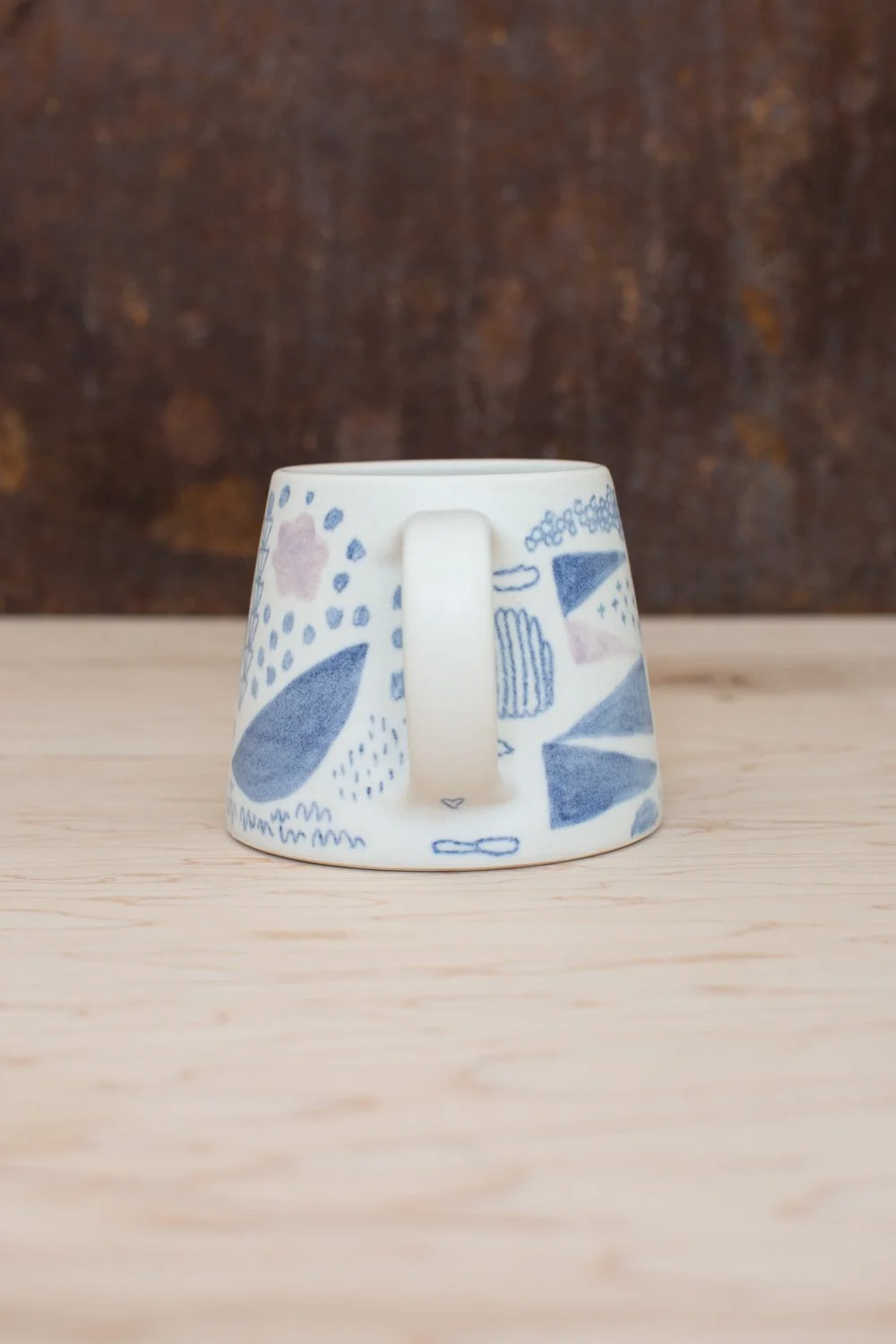 Hand-thrown porcelain mug with blue and pink illustrations.