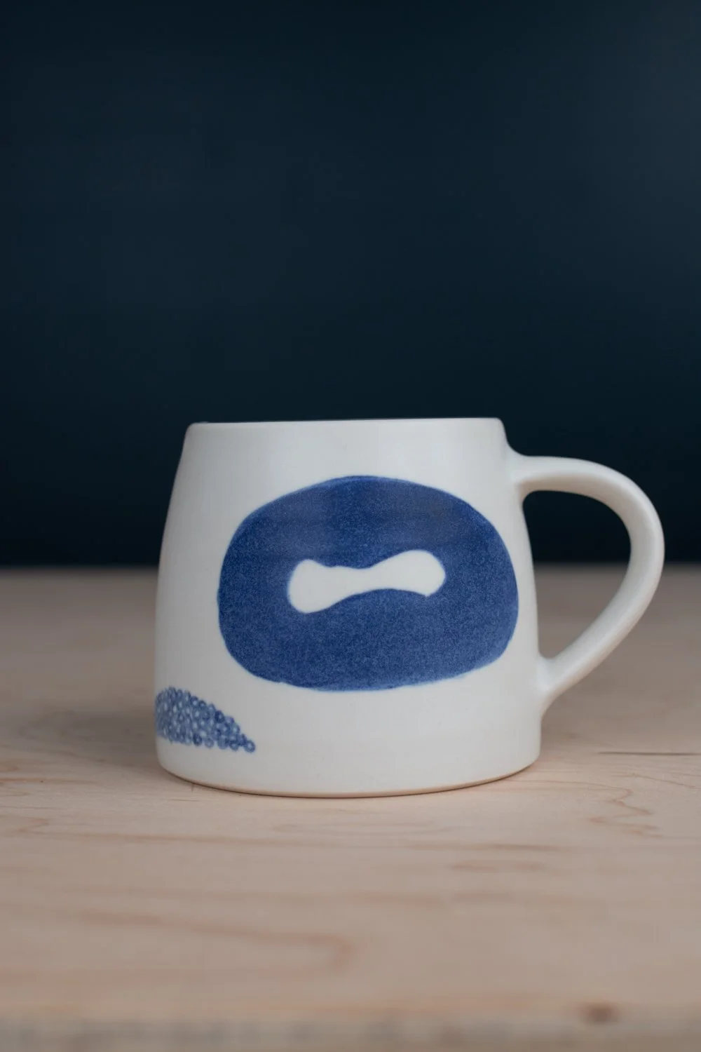 Hand-thrown porcelain mug with blue illustrations painted on the surface.