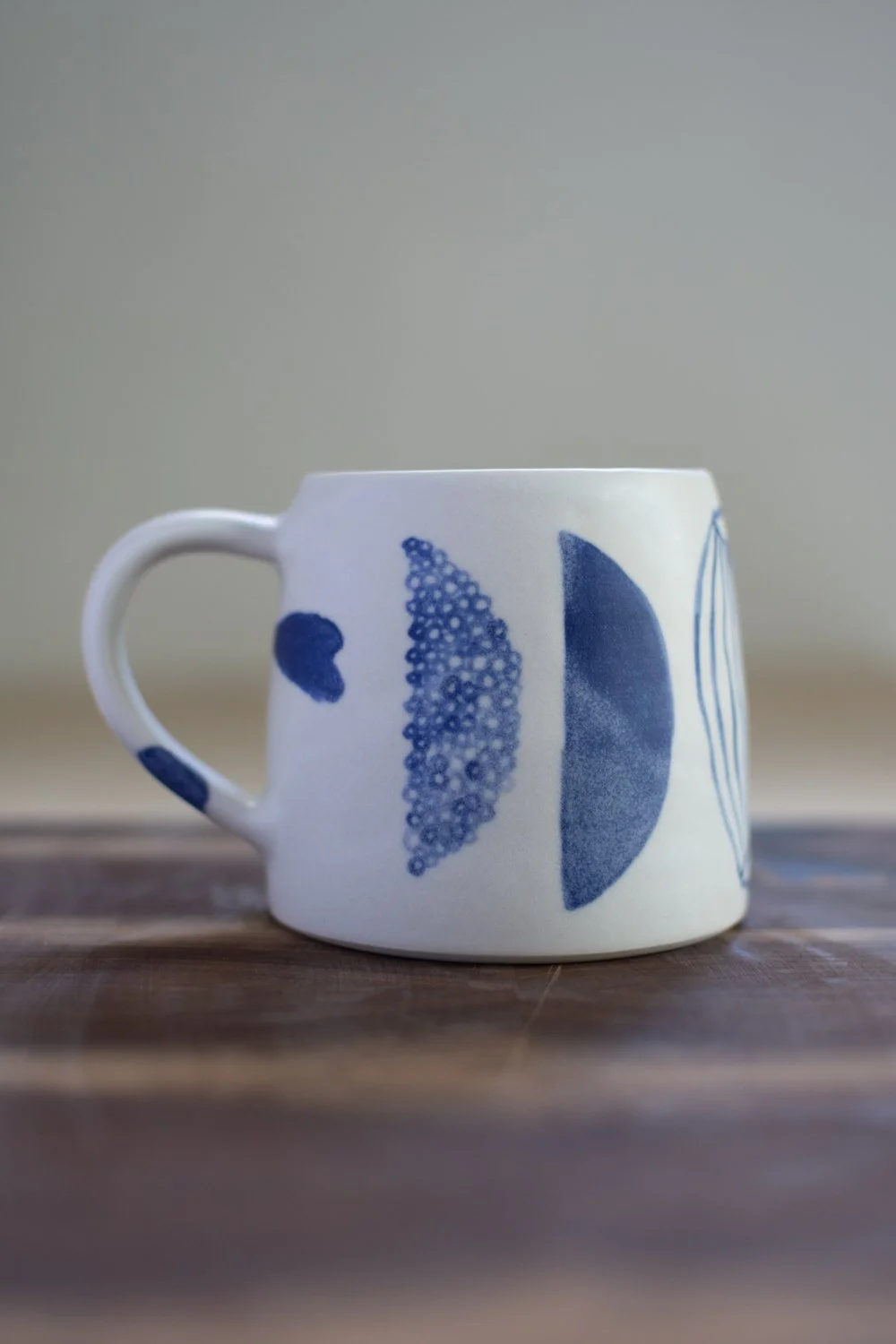 Hand-thrown porcelain mug with blue illustrations painted on the surface.