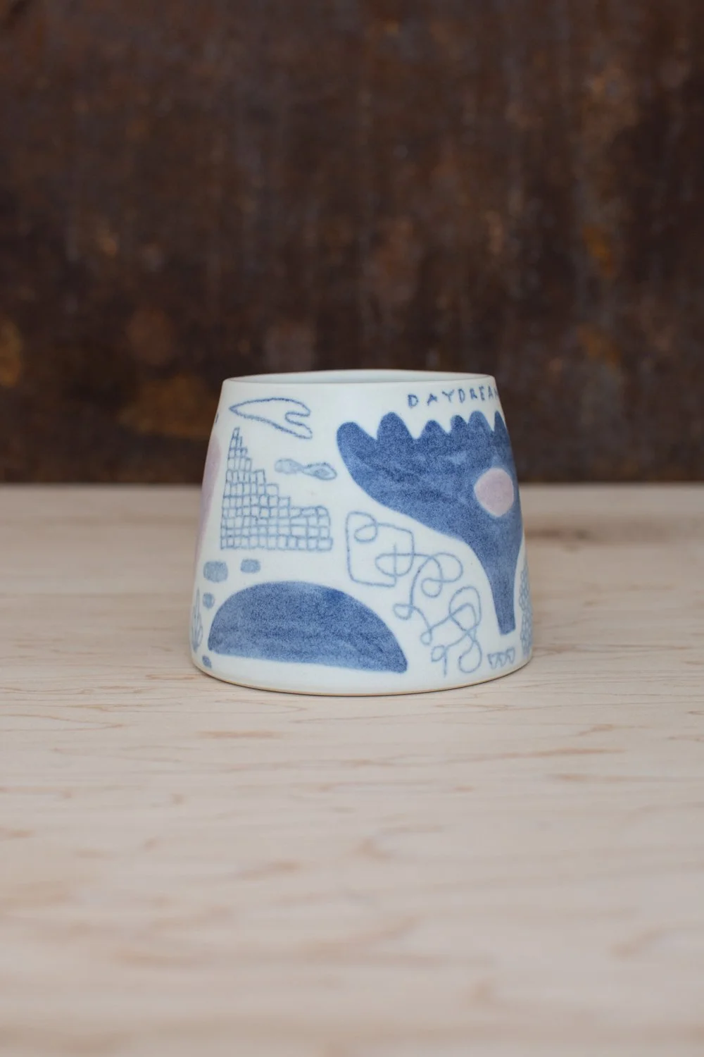 Hand-thrown porcelain mug with blue illustrations painted on the surface.
