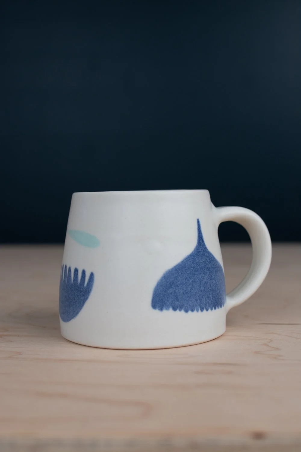 Hand-thrown porcelain mug with blue illustrations painted on the surface.