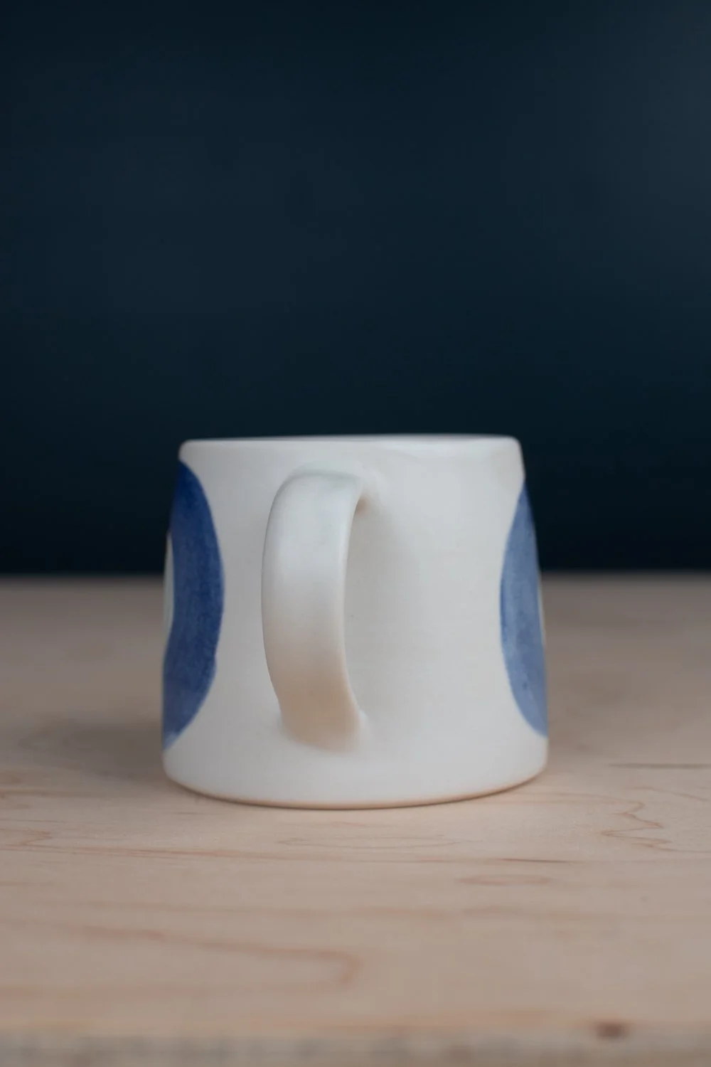 Hand-thrown porcelain mug with blue illustrations painted on the surface.