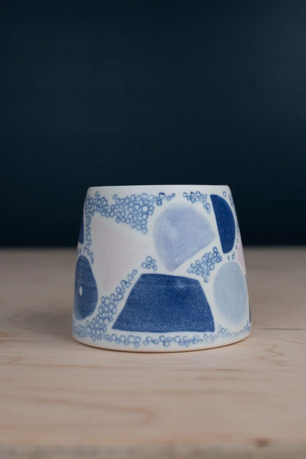 Hand-thrown porcelain mug with blue illustrations painted on the surface.