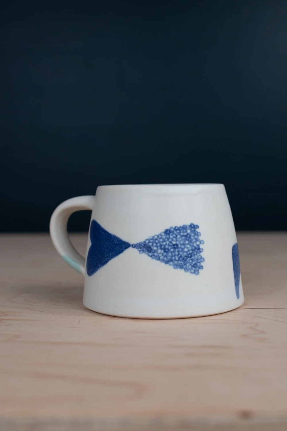 Hand-thrown porcelain mug with blue illustrations painted on the surface.