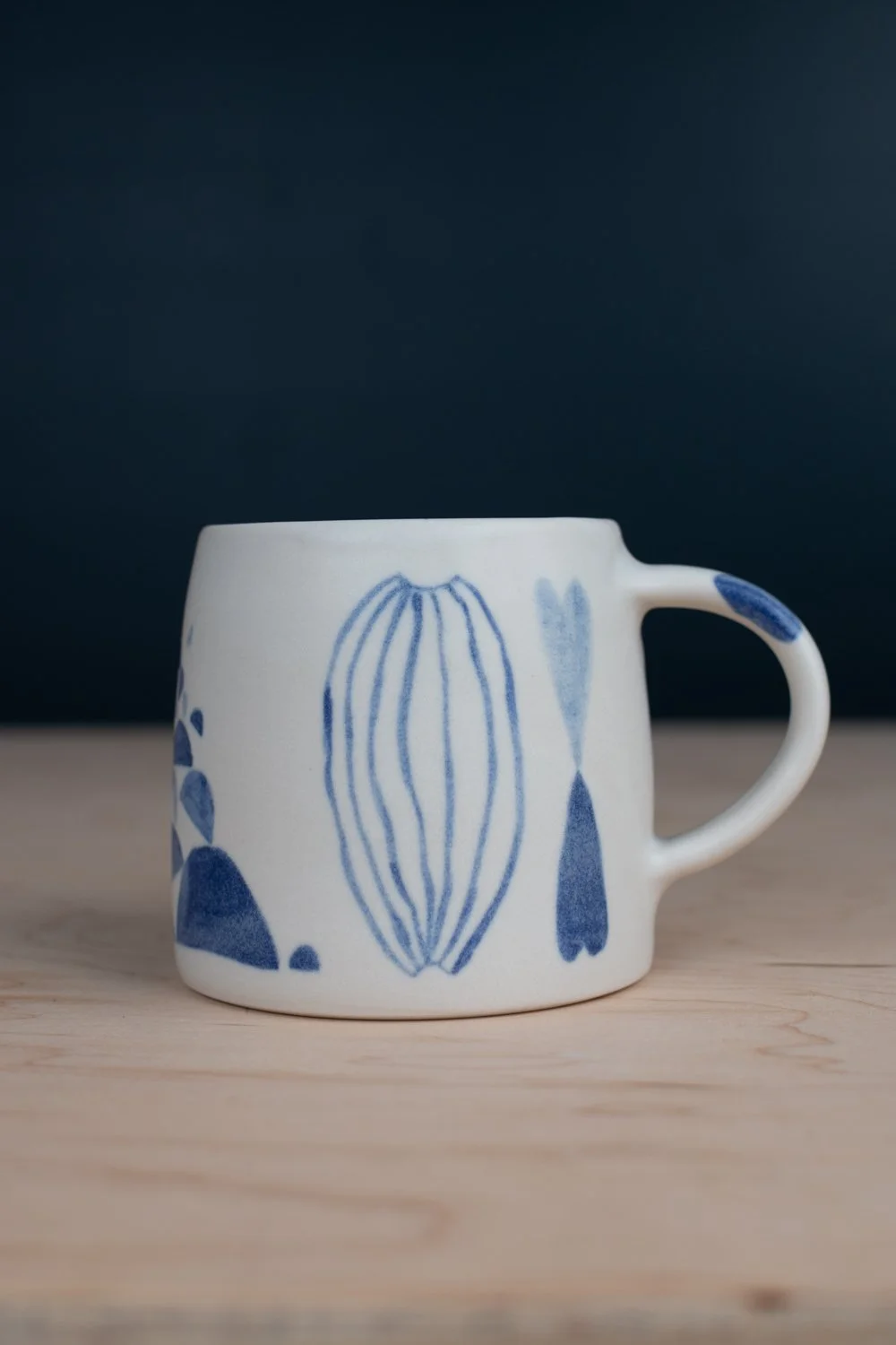 Hand-thrown porcelain mug with blue illustrations painted on the surface.