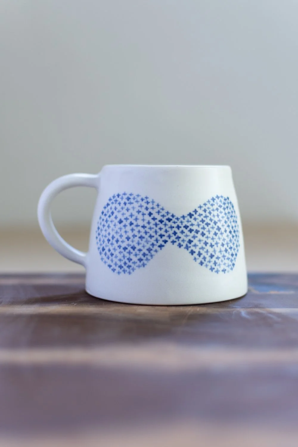 Hand-thrown porcelain mug with blue illustrations painted on the surface.