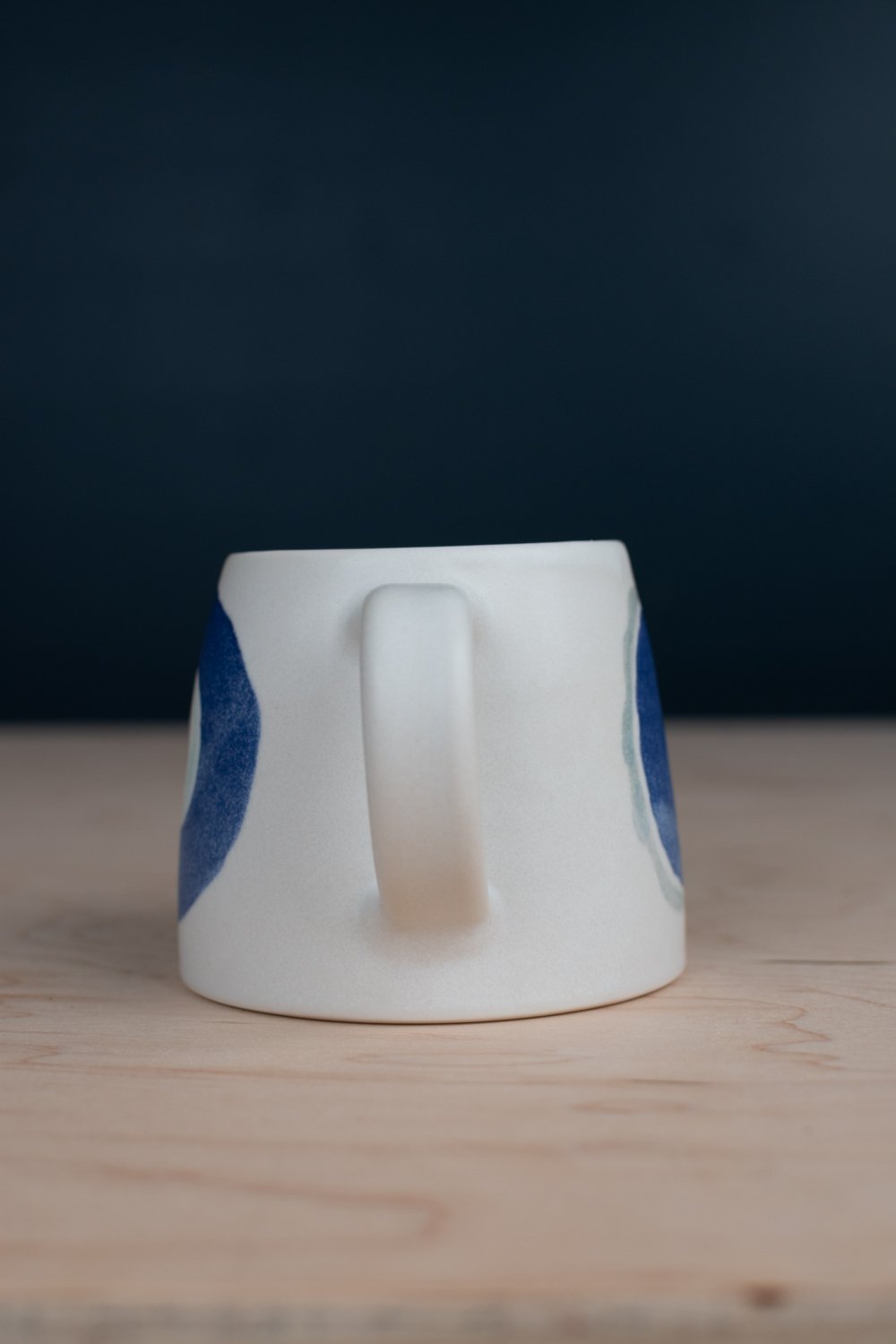 Hand-thrown porcelain mug with blue illustrations painted on the surface.