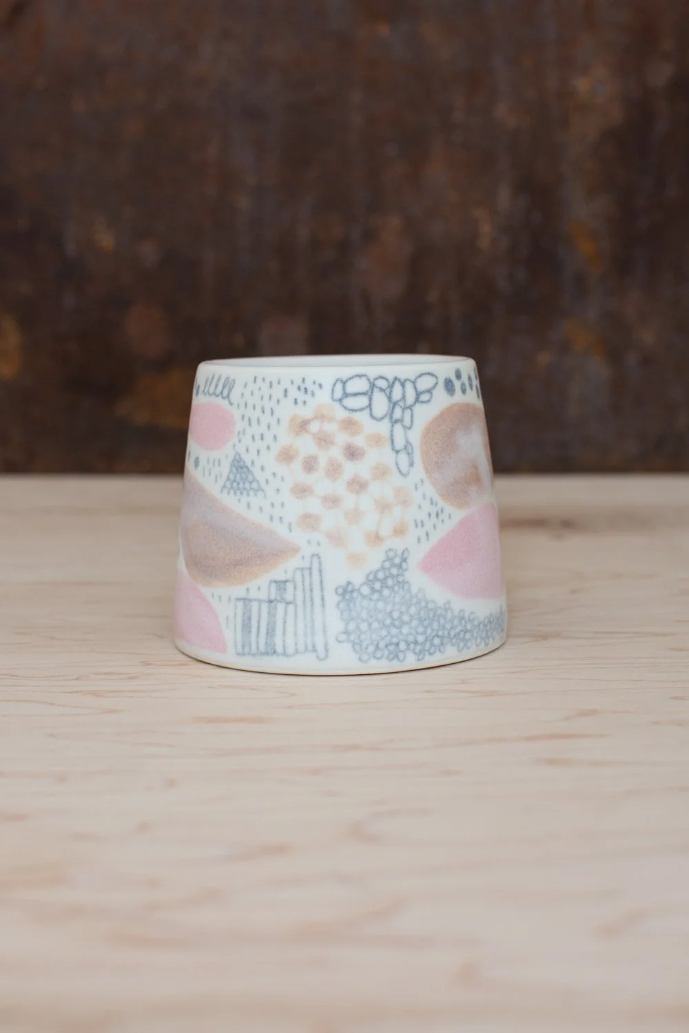Hand-thrown porcelain mug with pink and ochre illustrations painted on the surface.