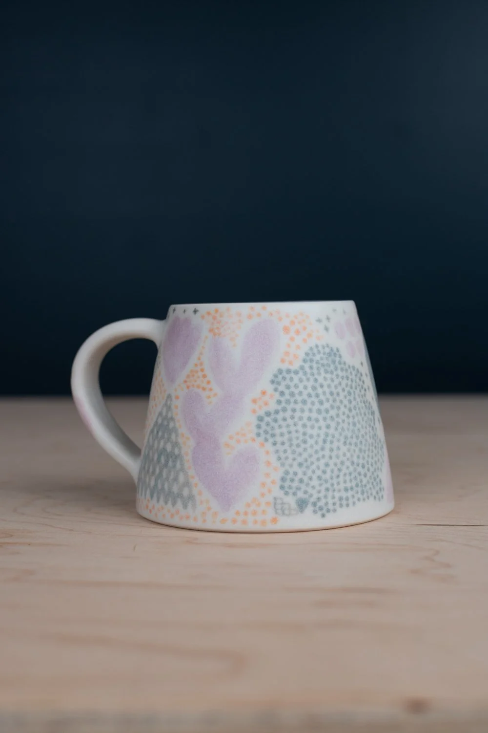 Hand-thrown porcelain mug with green, yellow, and lilac illustrations painted on the surface.