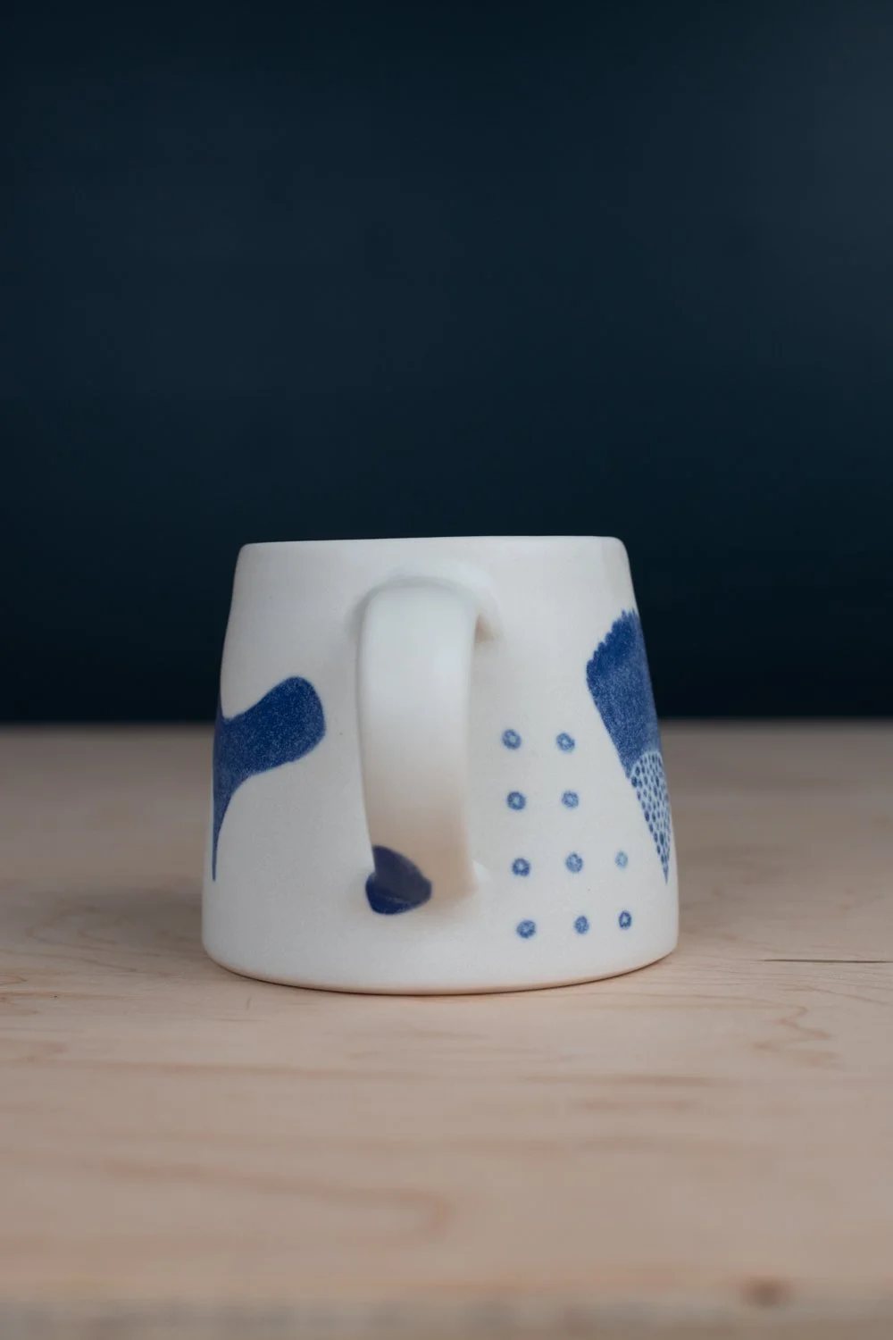 Hand-thrown porcelain mug with blue illustrations painted on the surface.
