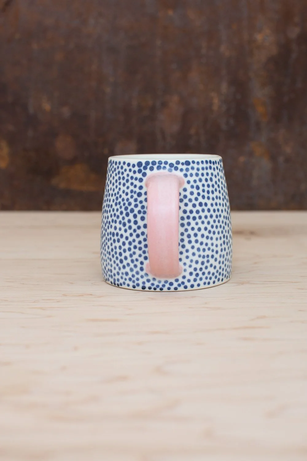 Hand-thrown porcelain mug with blue dots and a pink handle.