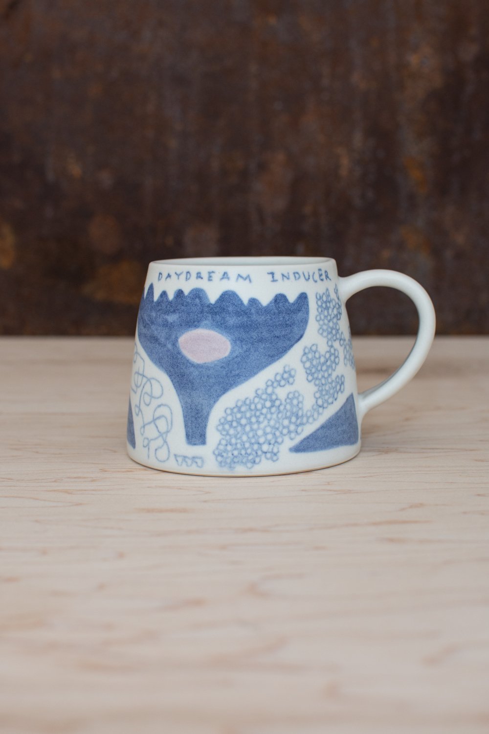 Hand-thrown porcelain mug with blue illustrations painted on the surface.