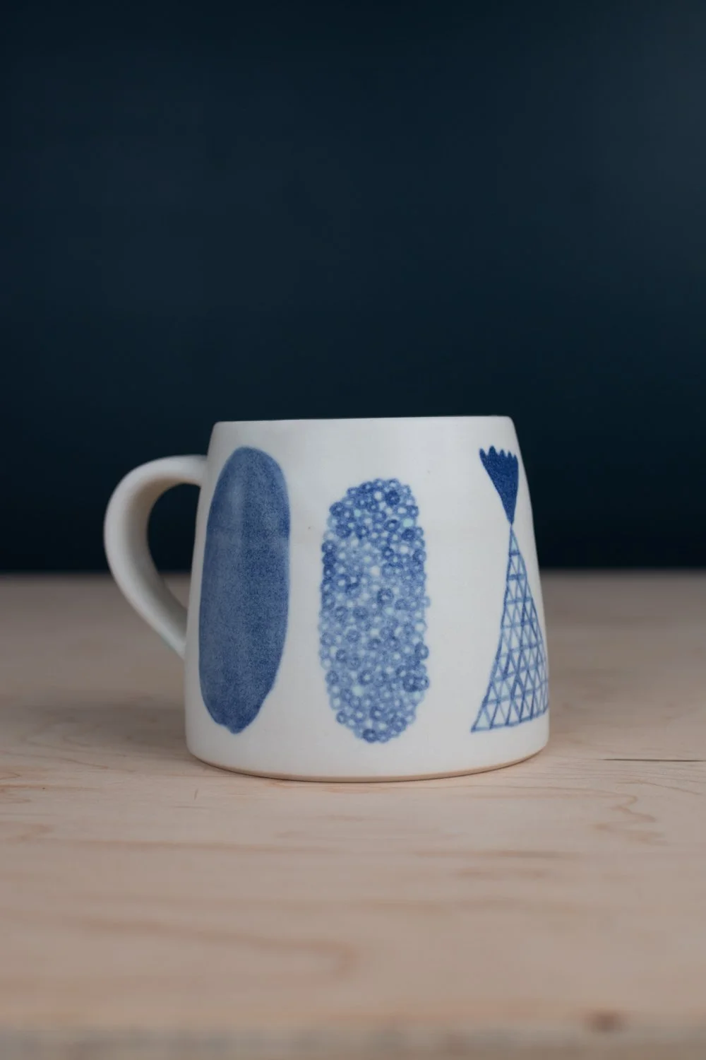 Hand-thrown porcelain mug with blue illustrations painted on the surface.
