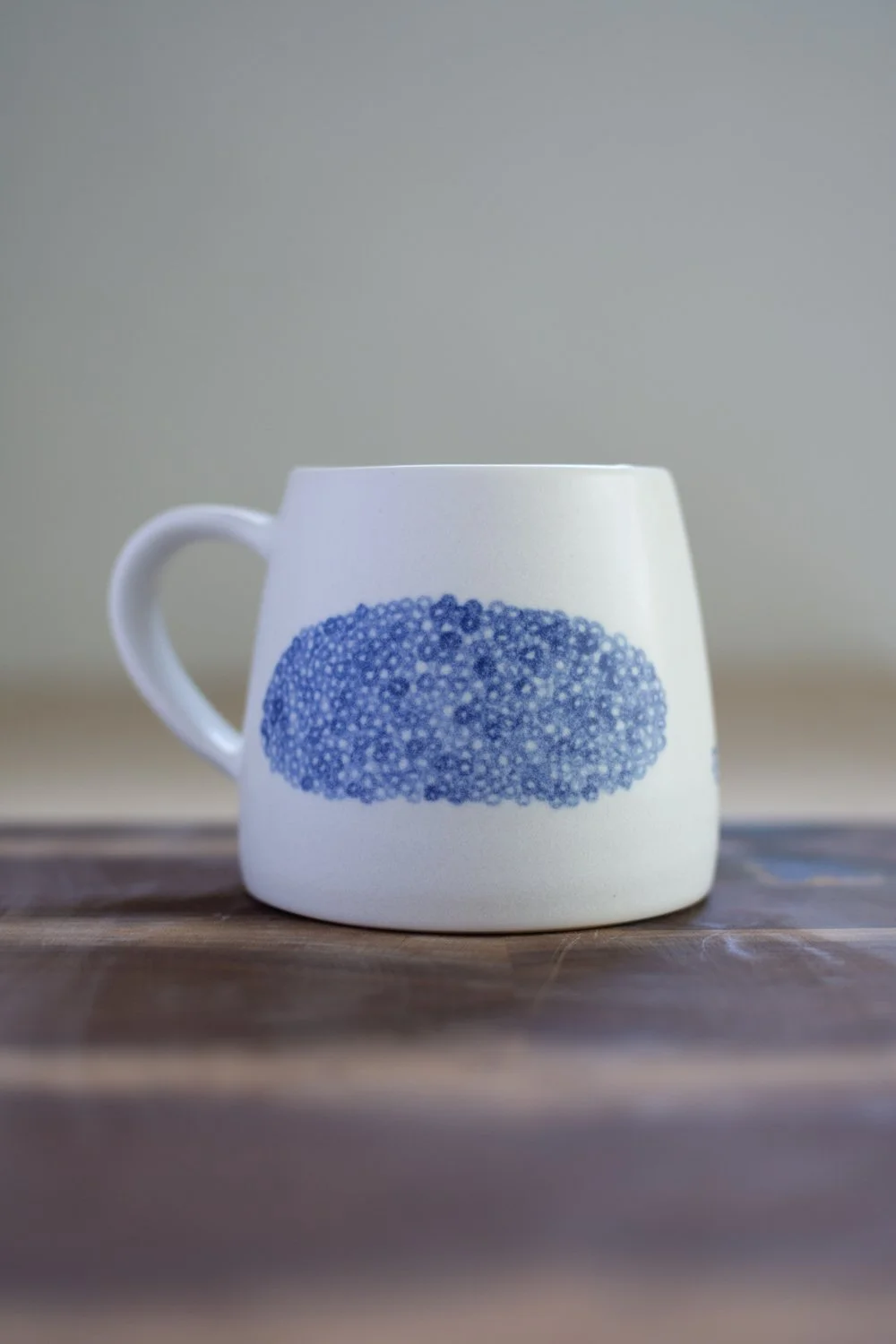 Hand-thrown porcelain mug with blue illustrations painted on the surface.