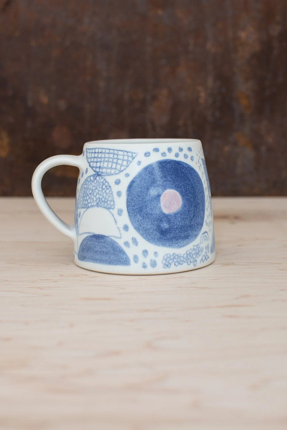 Hand-thrown porcelain mug with blue and purple illustrations painted on the surface.