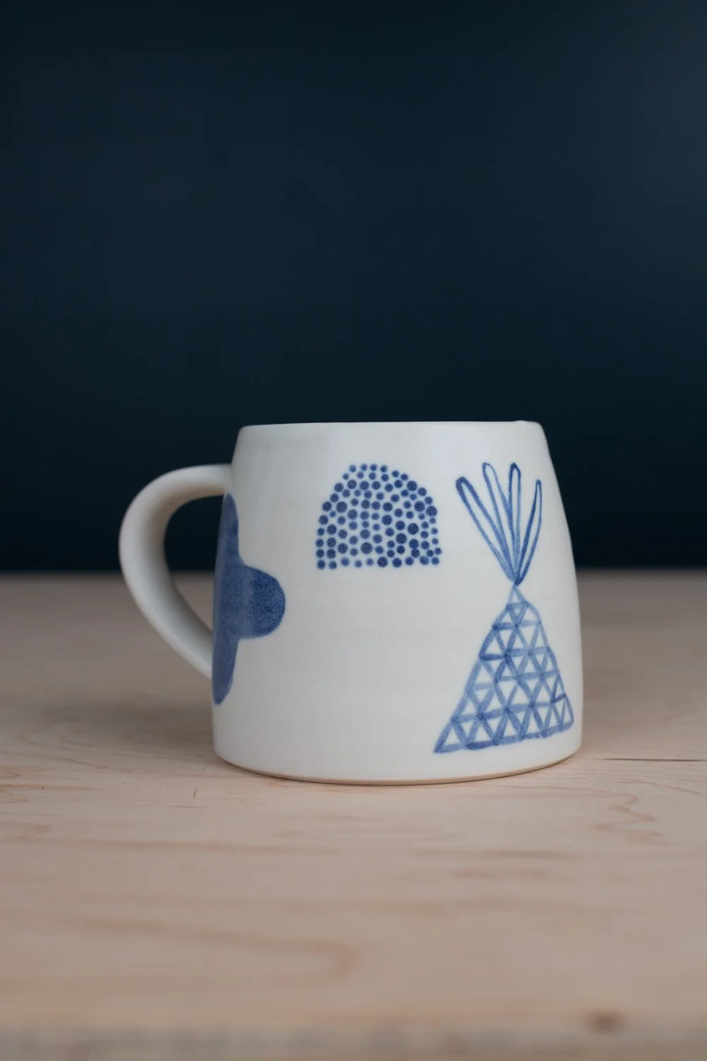 Hand-thrown porcelain mug with blue illustrations painted on the surface.