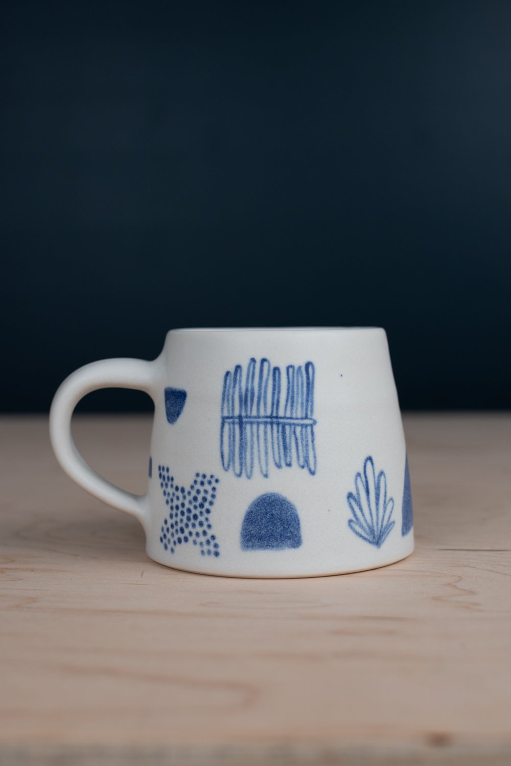 Hand-thrown porcelain mug with blue illustrations painted on the surface.