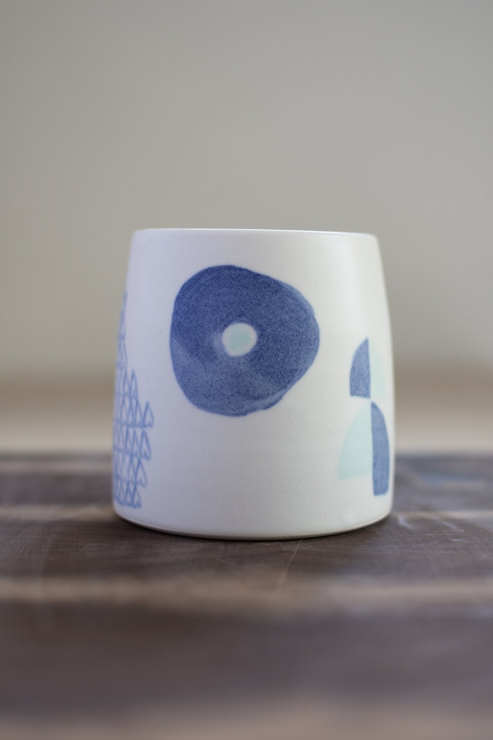 Hand-thrown porcelain mug with blue illustrations painted on the surface.