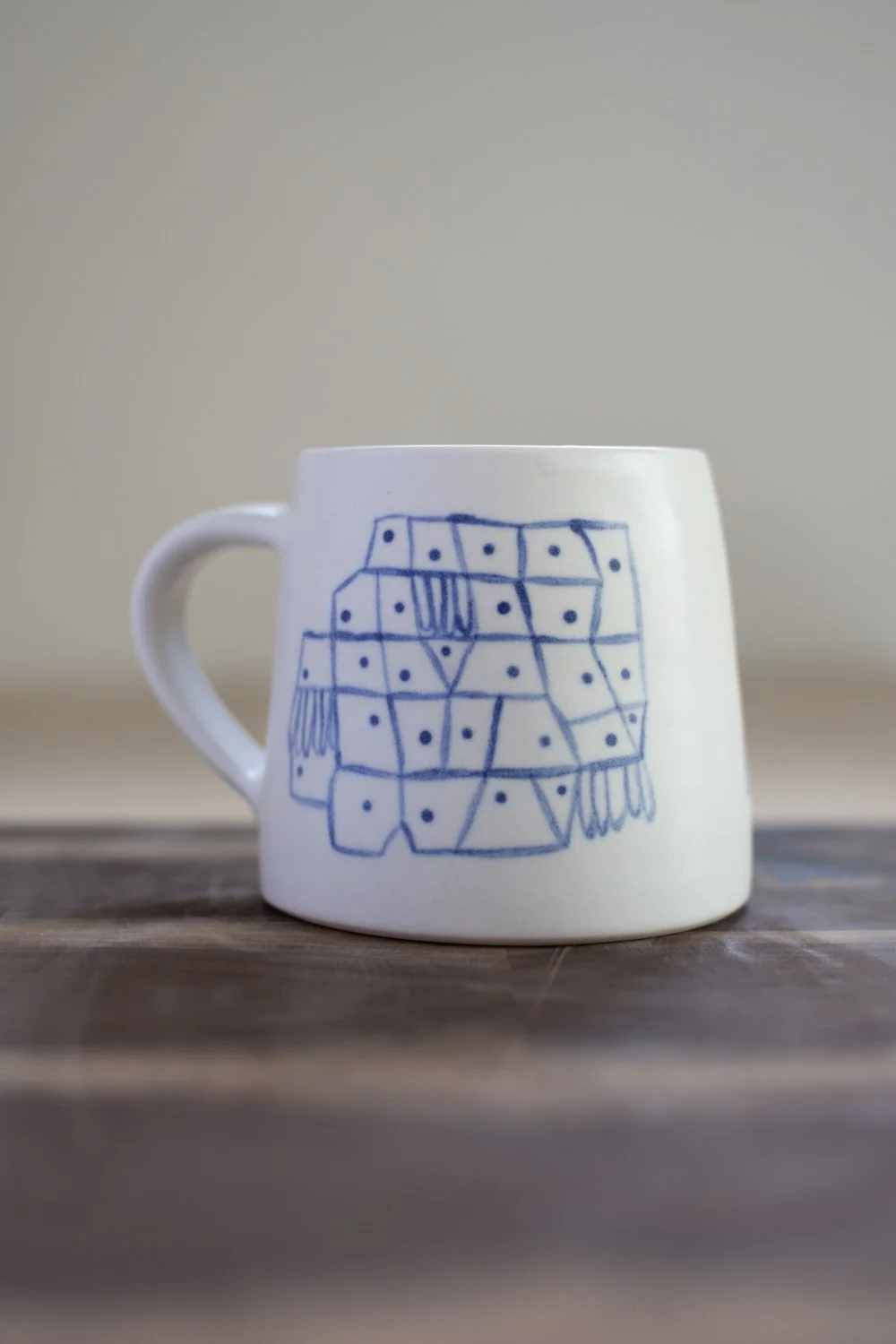 Hand-thrown porcelain mug with blue illustrations painted on the surface.