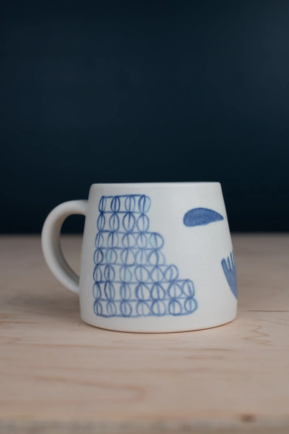 Hand-thrown porcelain mug with blue illustrations painted on the surface.