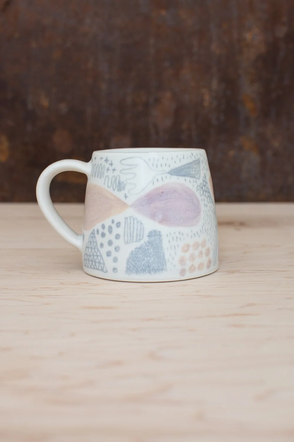 Hand-thrown porcelain mug with pink and ochre illustrations.