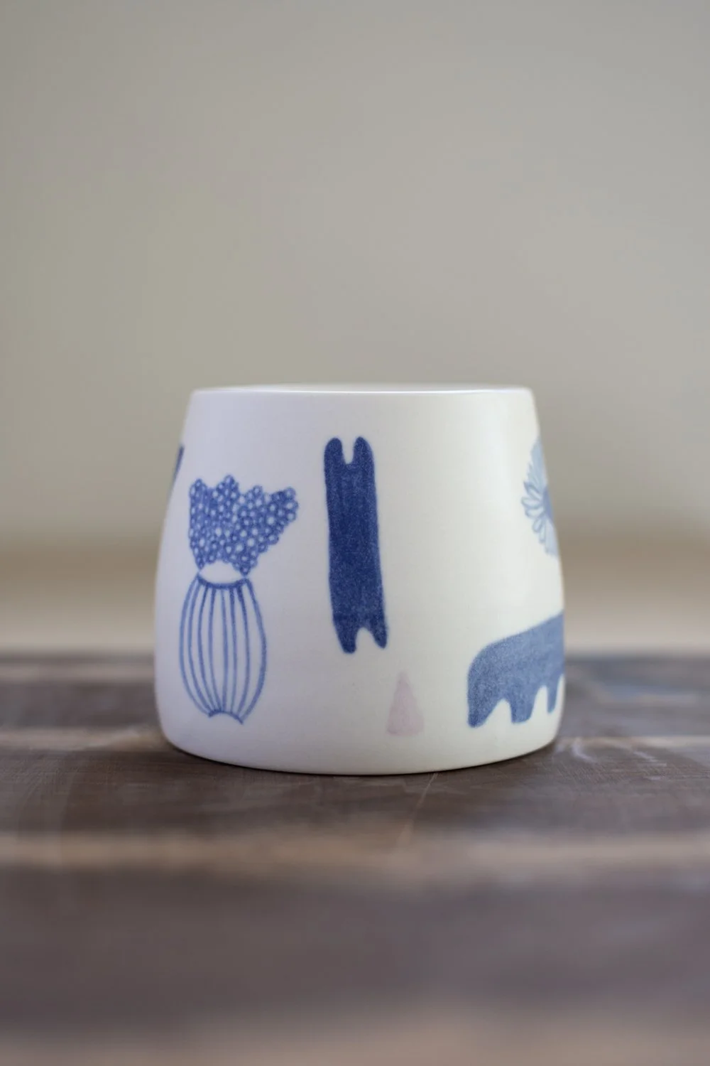 Hand-thrown porcelain mug with blue illustrations painted on the surface.