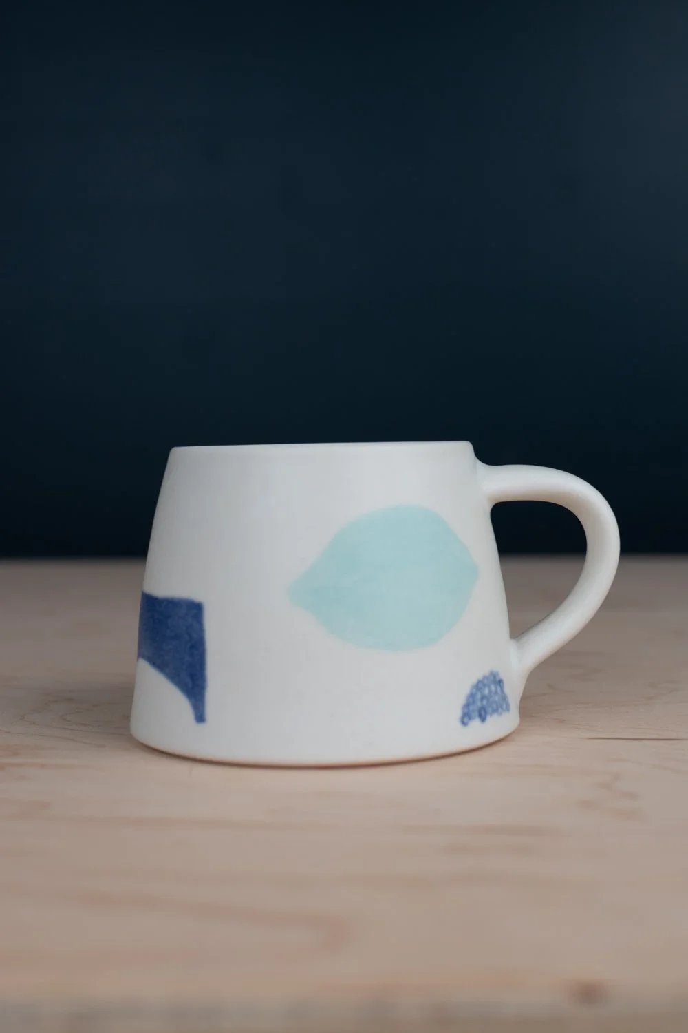 Hand-thrown porcelain mug with blue illustrations painted on the surface.