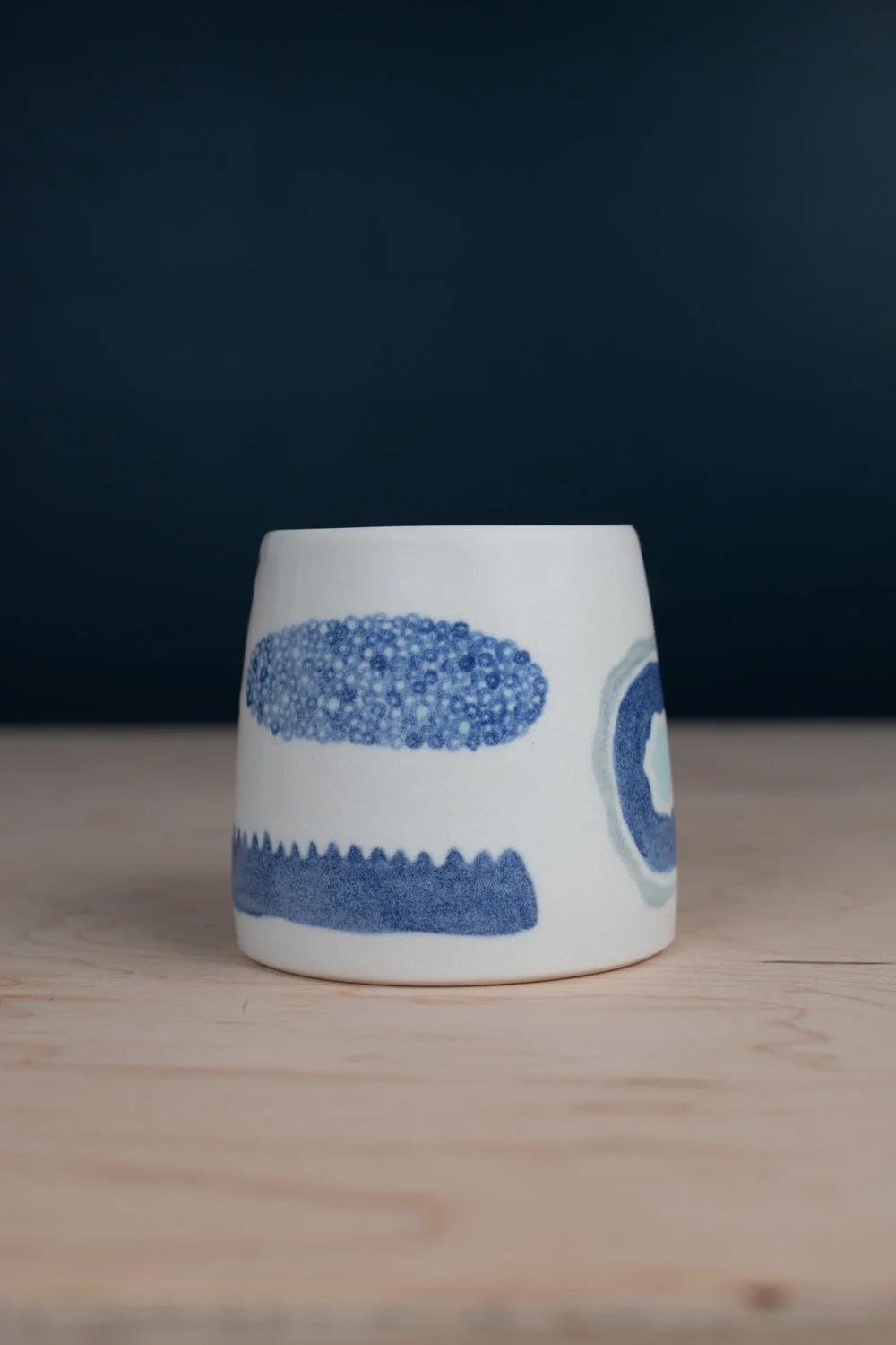 Hand-thrown porcelain mug with blue illustrations painted on the surface.